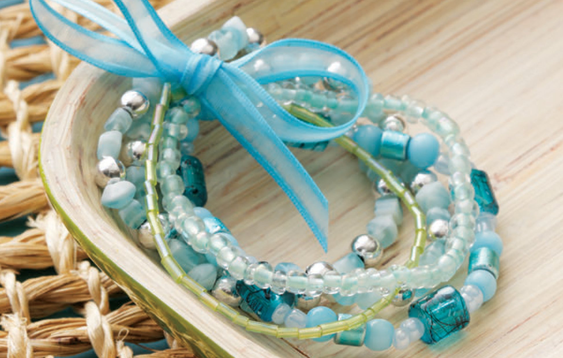 DIY Jewelry Learn the Basics by Leisure Arts features blue and silver beaded bracelets tied with a sheer blue ribbon, displayed on a wooden tray—ideal for beginner jewelry makers looking for easy projects.
