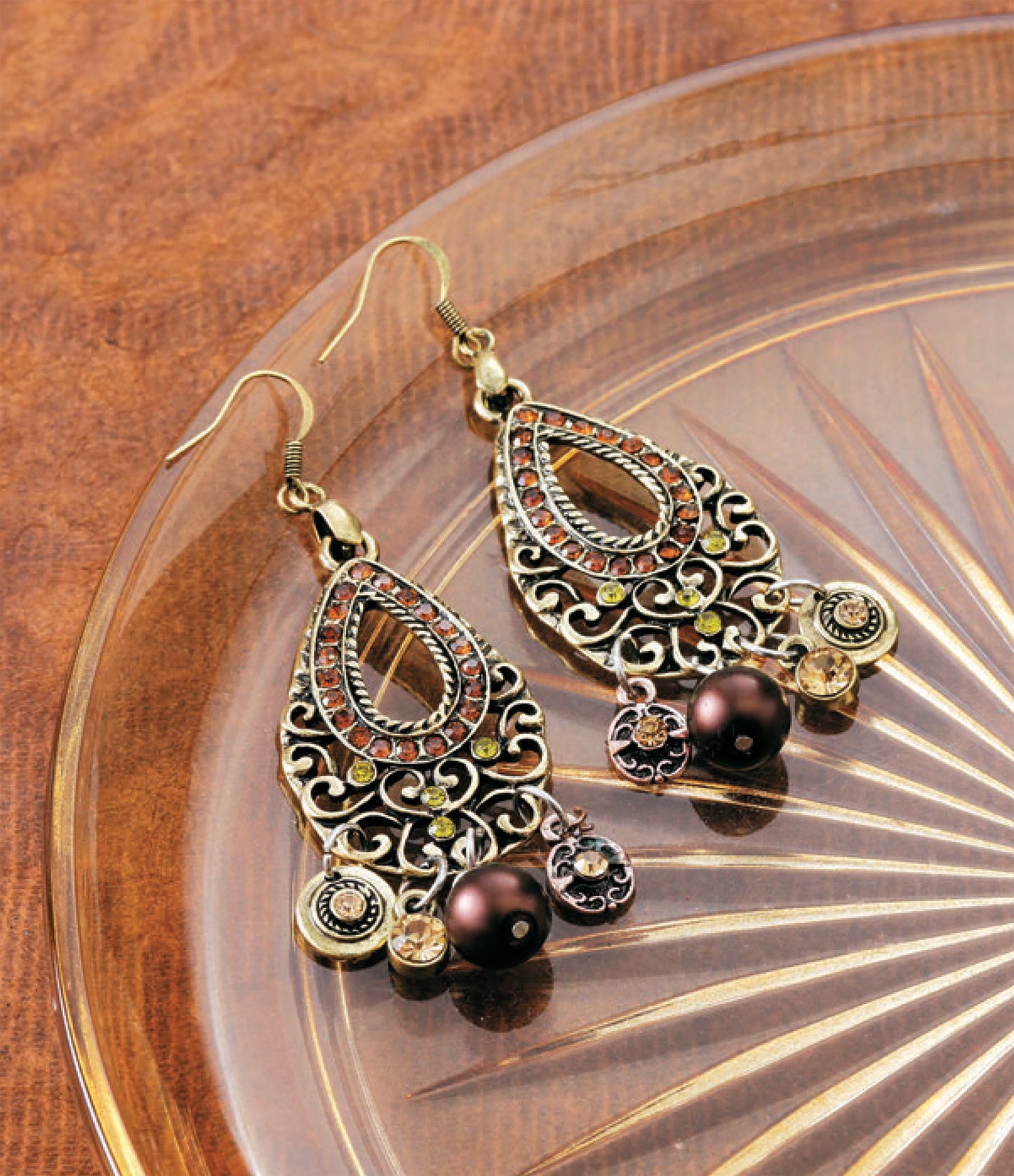 DIY Jewelry Learn the Basics by Leisure Arts features ornate gold earrings with filigree design and brown beads, ideal for beginners. Shown on a starburst-patterned glass dish.
