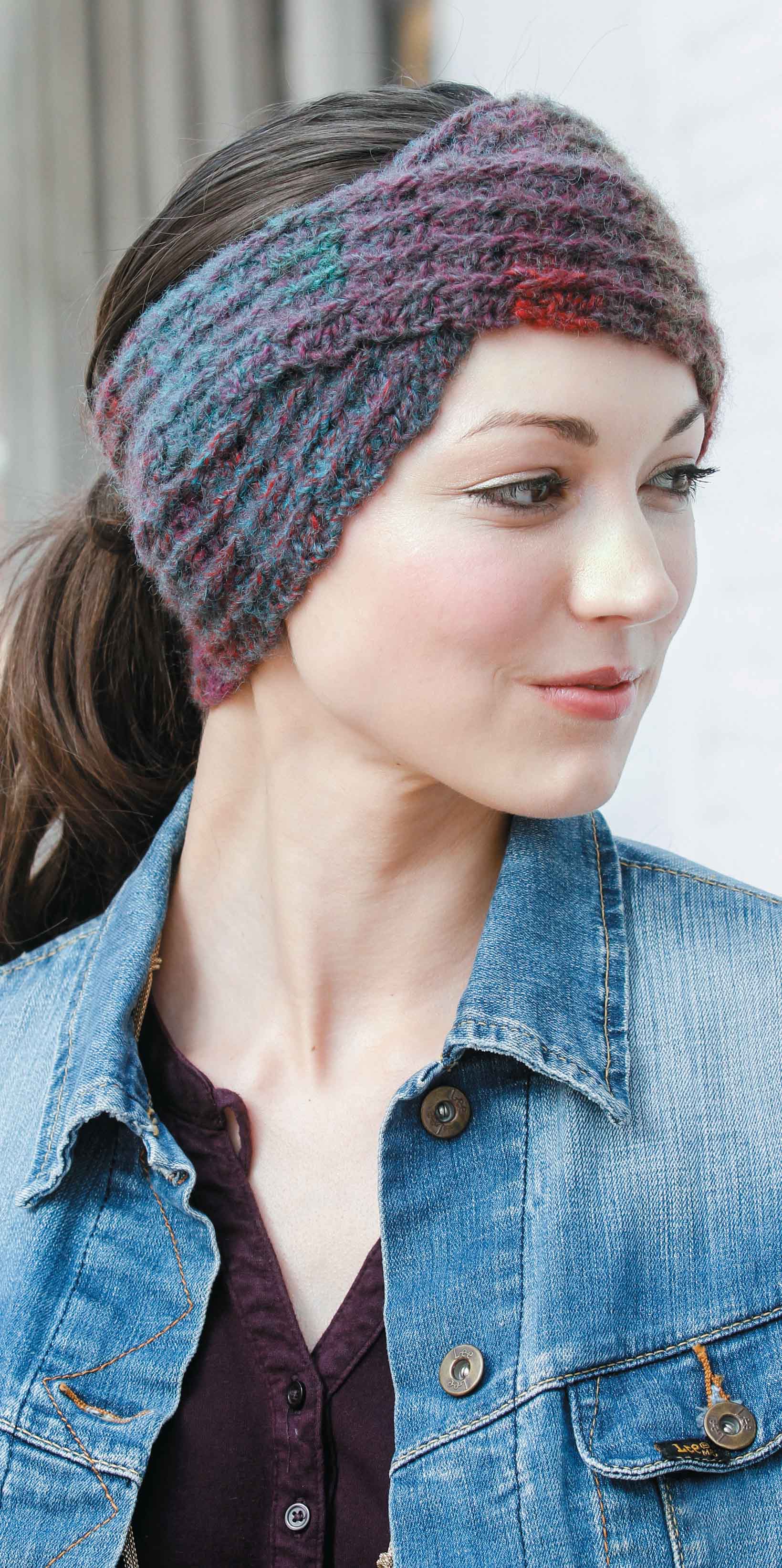 A woman with dark hair pulled back models a colorful headwrap from the Leisure Arts Slouchy Beanies and Headwraps Digital Download, paired with a denim jacket and dark shirt, giving inspiration for beginner crocheters.