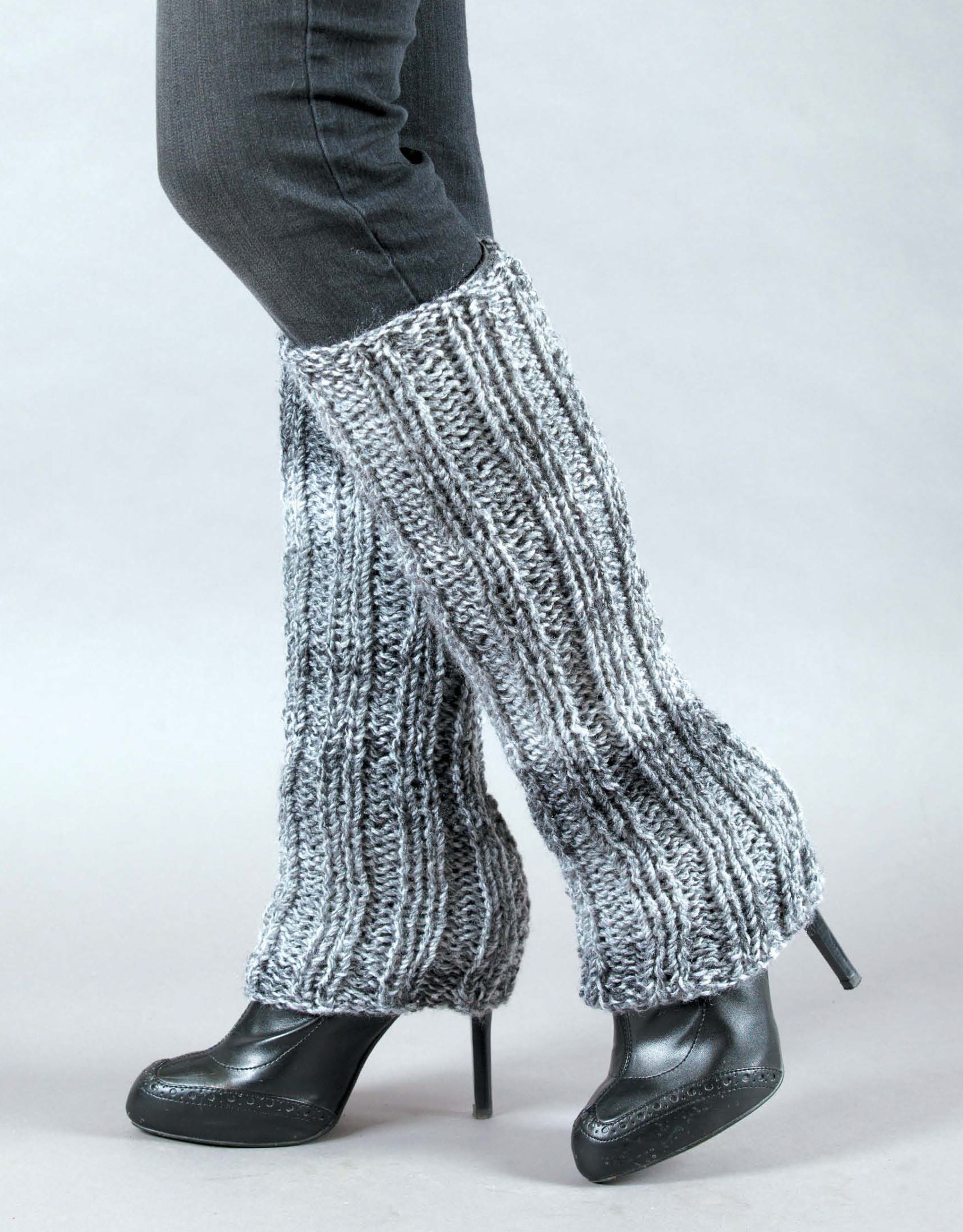 A person wears black heels, dark pants, and flared gray chunky-knit leg warmers—perfect inspiration for beginner knitters. Shown: "Learn to Knit, Now! Digital Download" by Leisure Arts. The background is plain and light-colored.