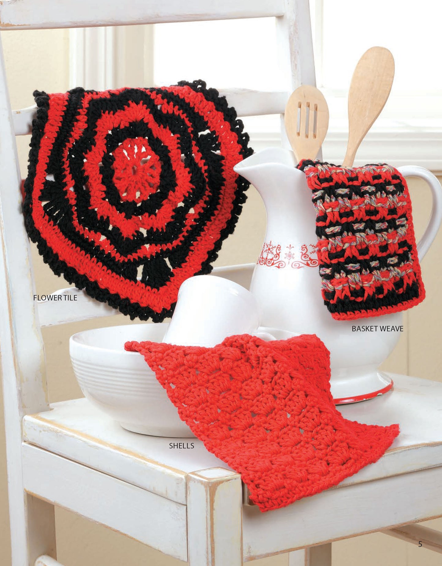 Three textured dishcloths from Leisure Arts’ “Dishcloths—A Super Collection for Home or Gifts! Digital Download” are displayed on white kitchenware and a chair, adding colorful accents with red and black patterns.