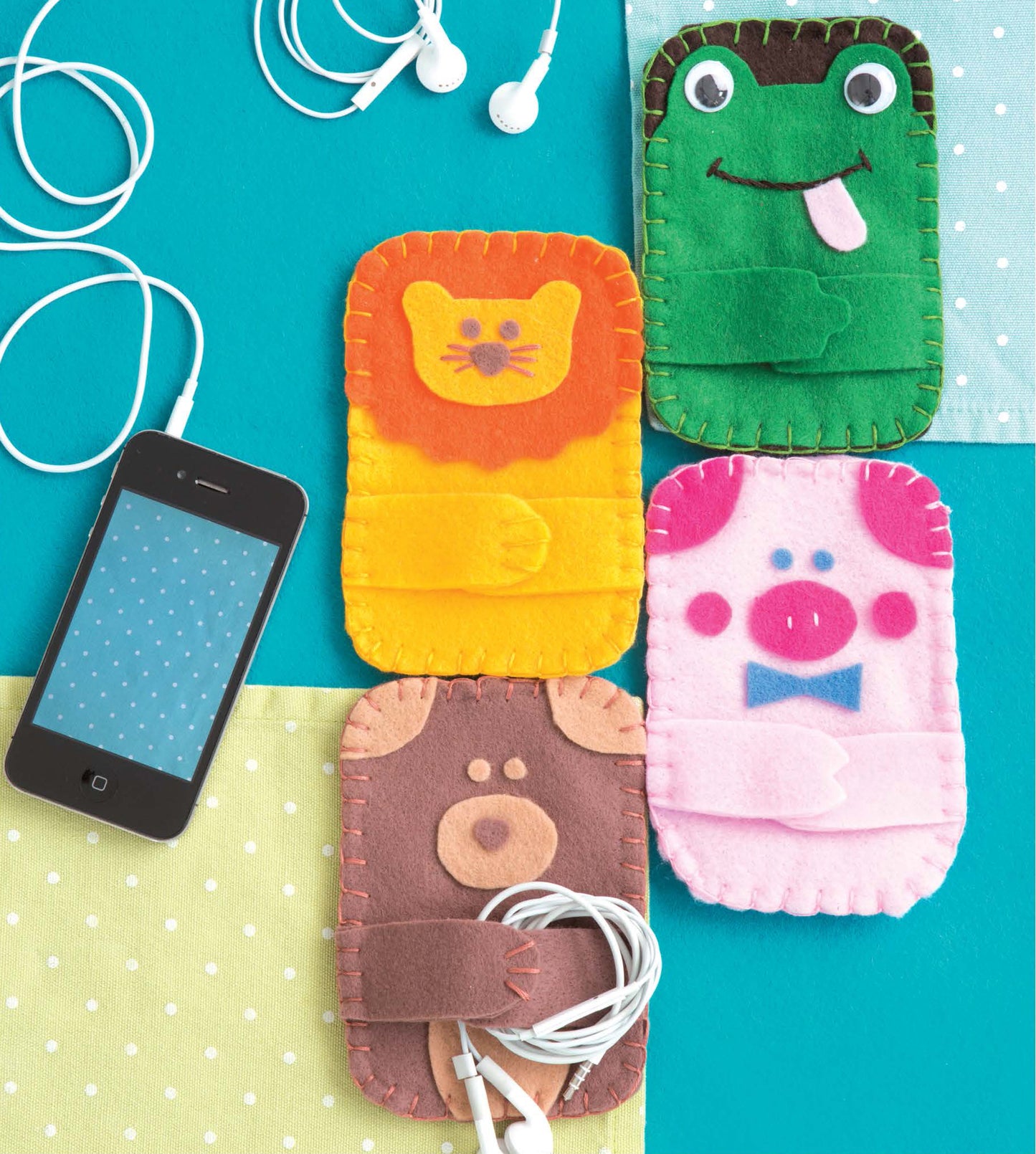 Leisure Arts’ “Crafting with Felt” features four colorful animal-shaped phone cases—a lion, frog, pig, and bear—with stitched details. Displayed among baby accessories and gadgets, the cute cases add charm to any setting.