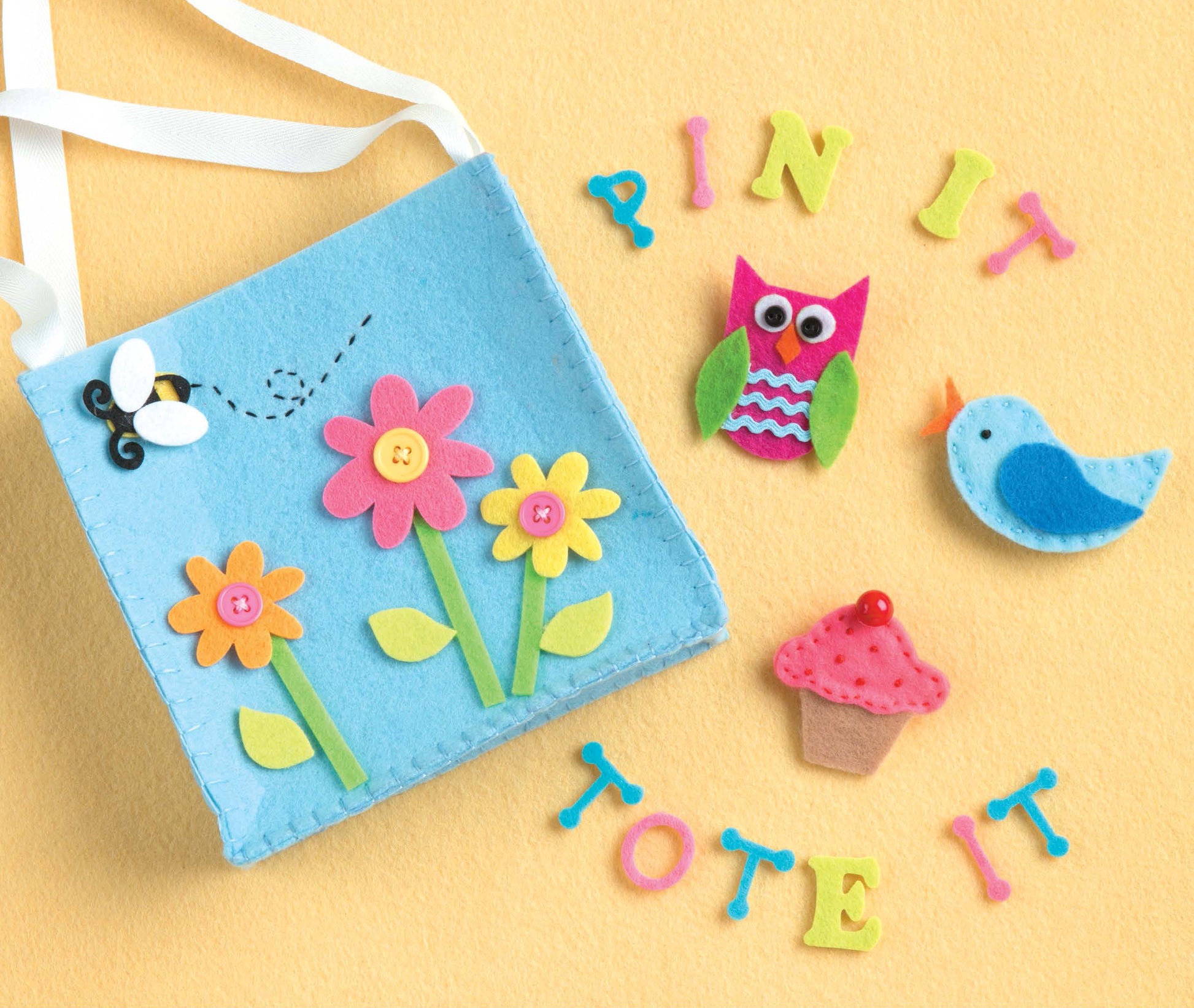 The "Crafting with Felt" kit by Leisure Arts features a blue bag decorated with colorful felt flowers, a bee, and playful shapes—ideal for storing baby accessories or kids toys, all shown on a bright yellow background.