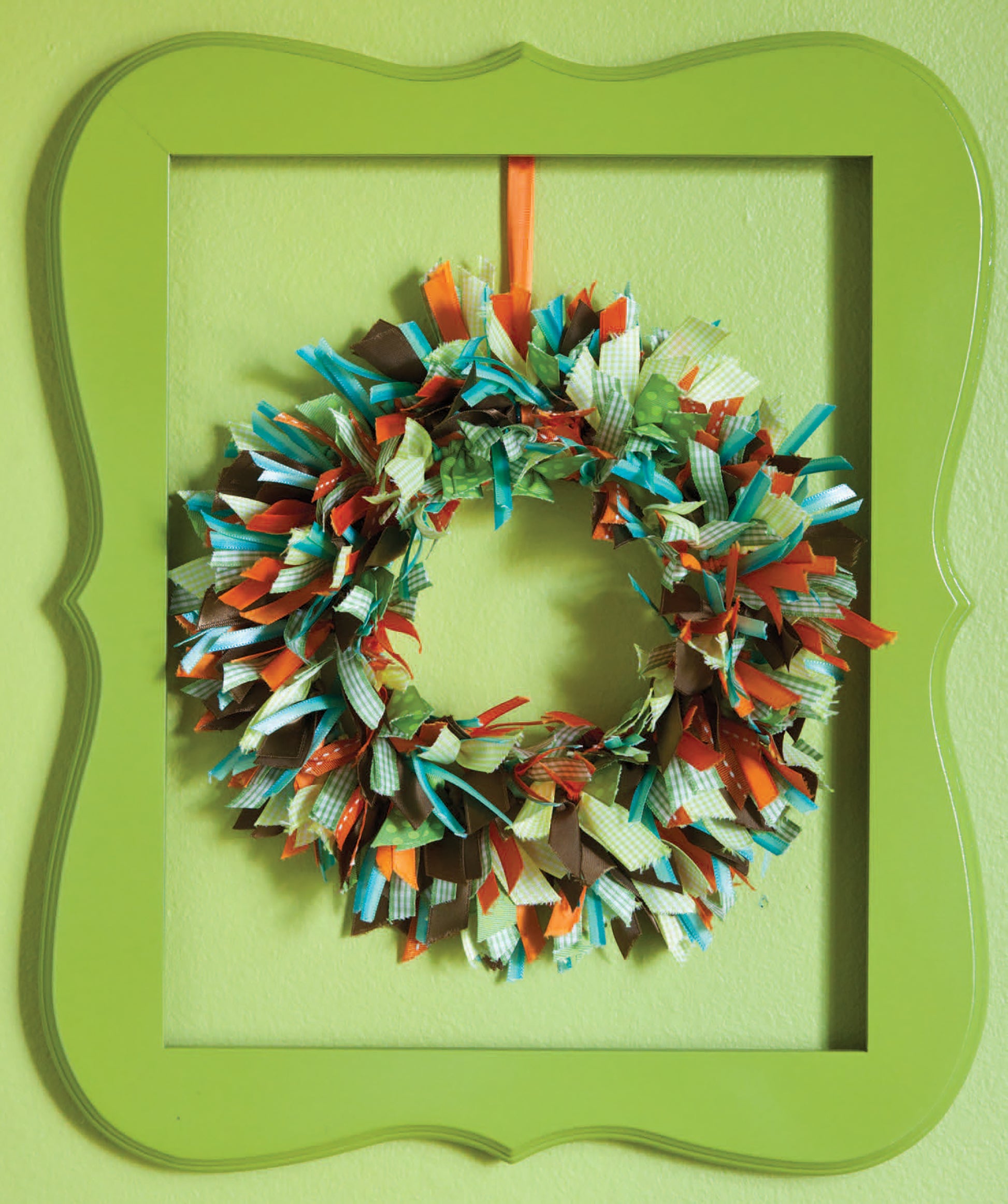 Add a unique touch to your home decor with the "Crafting with Buttons and Ribbons" kit by Leisure Arts—a colorful wreath of fabric strips in green, blue, orange, and brown framed in bright green on a light green wall.