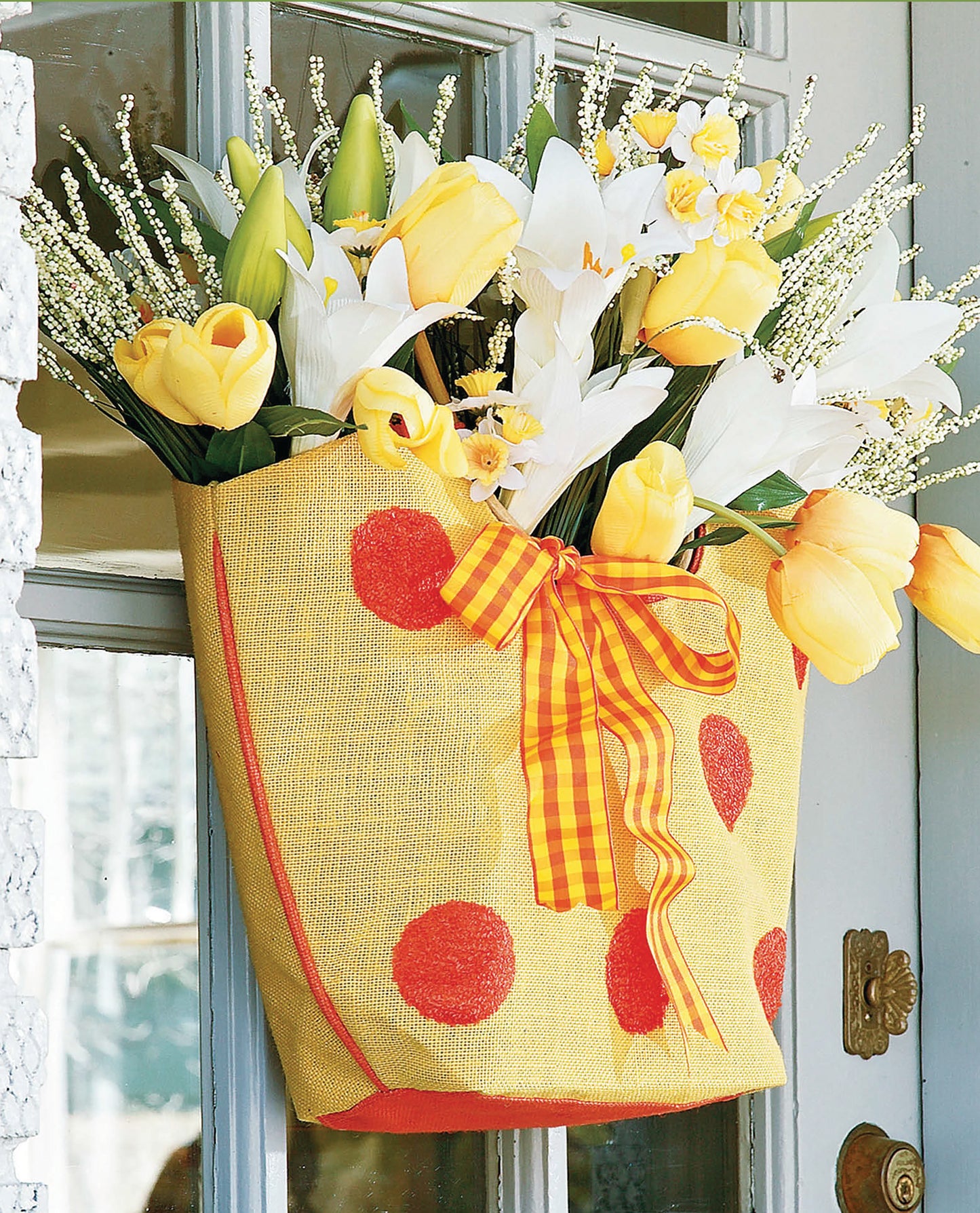 The "Crafting with Florals" kit by Leisure Arts features a yellow polka-dotted bag with an orange bow, filled with yellow tulips and white lilies—creating a cheerful flower arrangement for home decor.