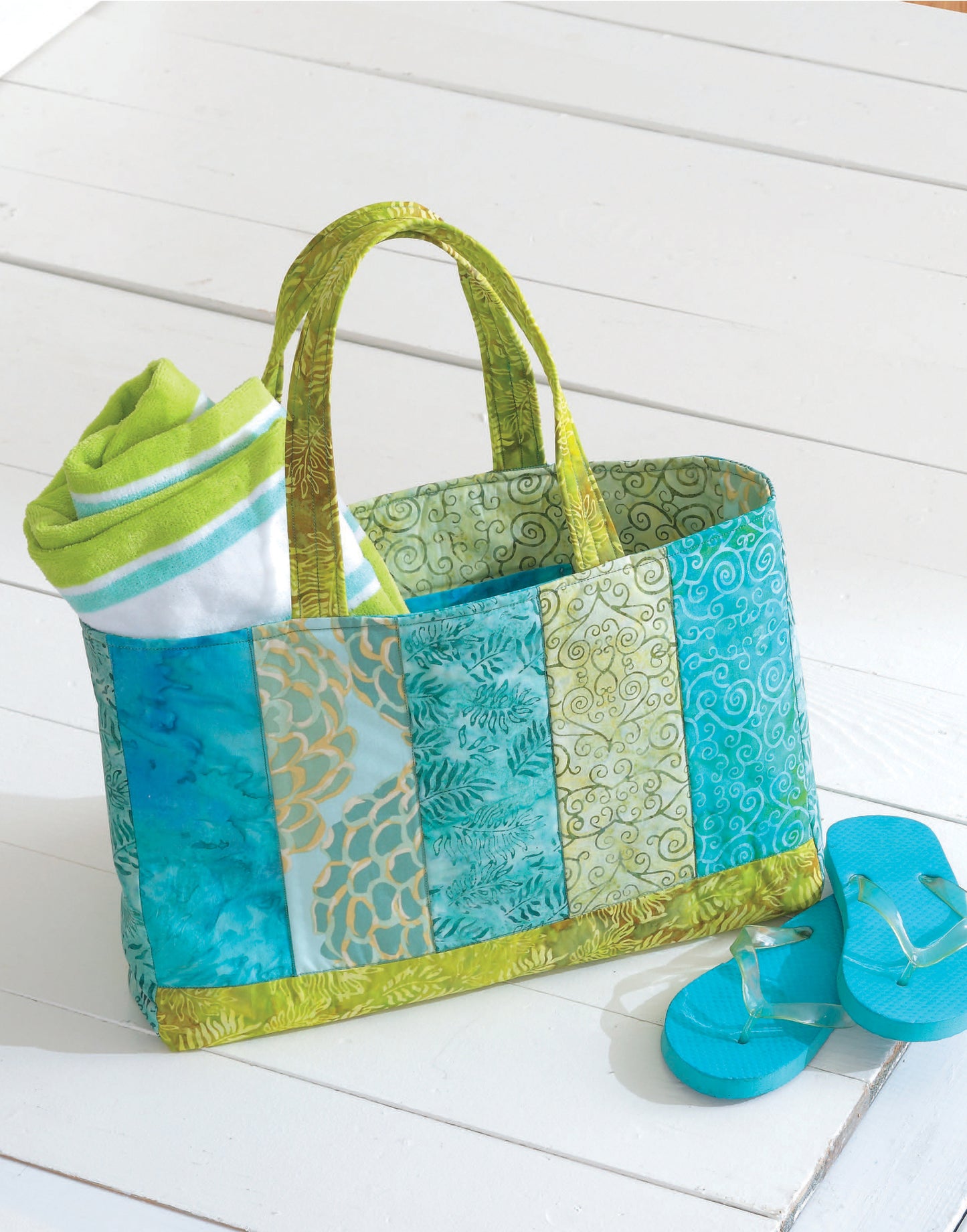 The Leisure Arts Fat Quarter Bag, inspired by quilted designs, holds a green and white striped towel on a white wood floor next to bright blue flip-flops.