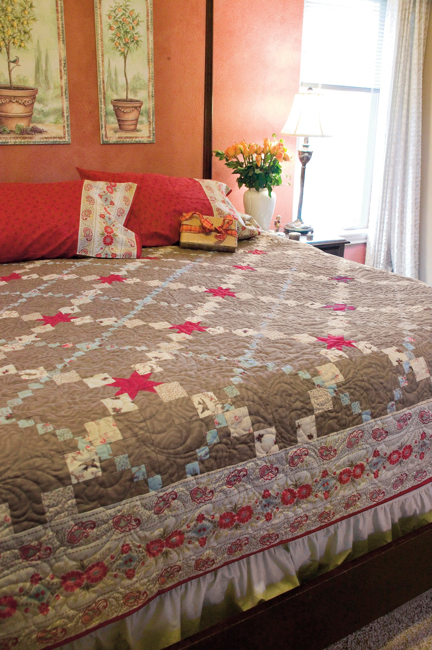 A neatly made bed with a gray, red, and white quilt sets the scene for creativity. With "Simple Beginner Quilts Digital Download" from Leisure Arts and inspiring tree prints, it’s perfect for adventurous quilting beginners.