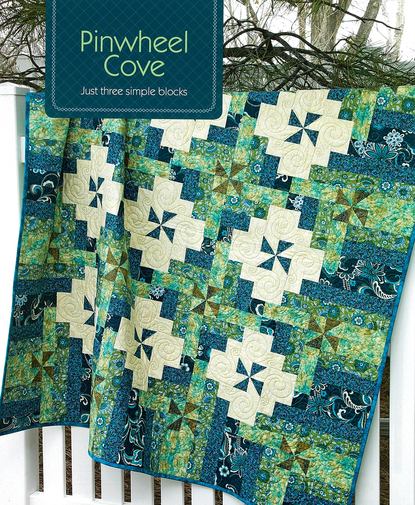 A vibrant quilt with blue, green, and cream pinwheel and star patterns hangs on a white fence. Inspired by Quiltmaker Magazine, Simple Patchwork Quilts—Best of Quiltmaker by Leisure Arts is perfect for beginners. Trees appear in the background.