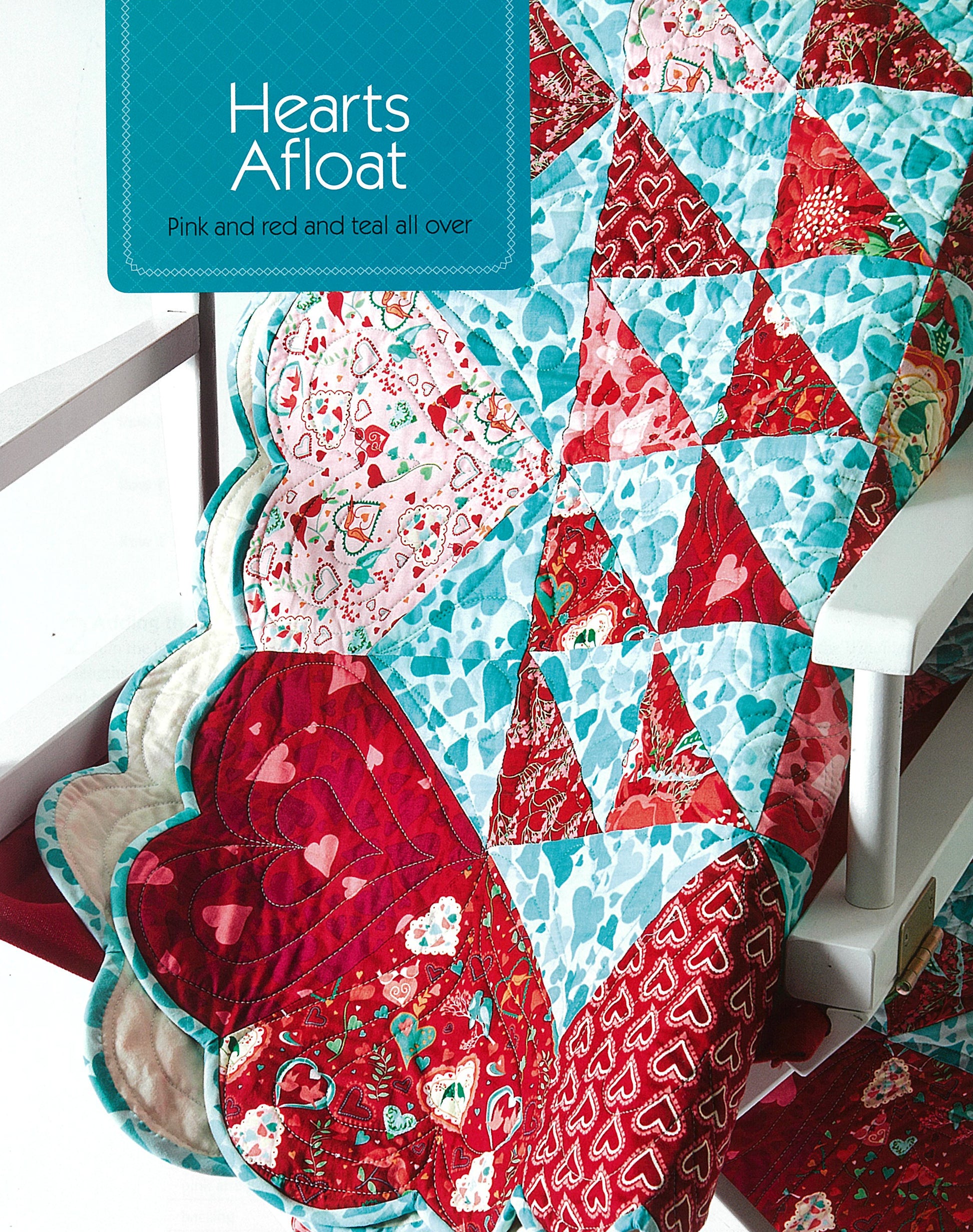 A quilt with pink, red, and teal triangle and heart patterns from Leisure Arts’ Simple Patchwork Quilts—Best of Quiltmaker is draped over a white chair, featuring easy piecing for beginners and a scalloped heart edge. Sign: Hearts Afloat.