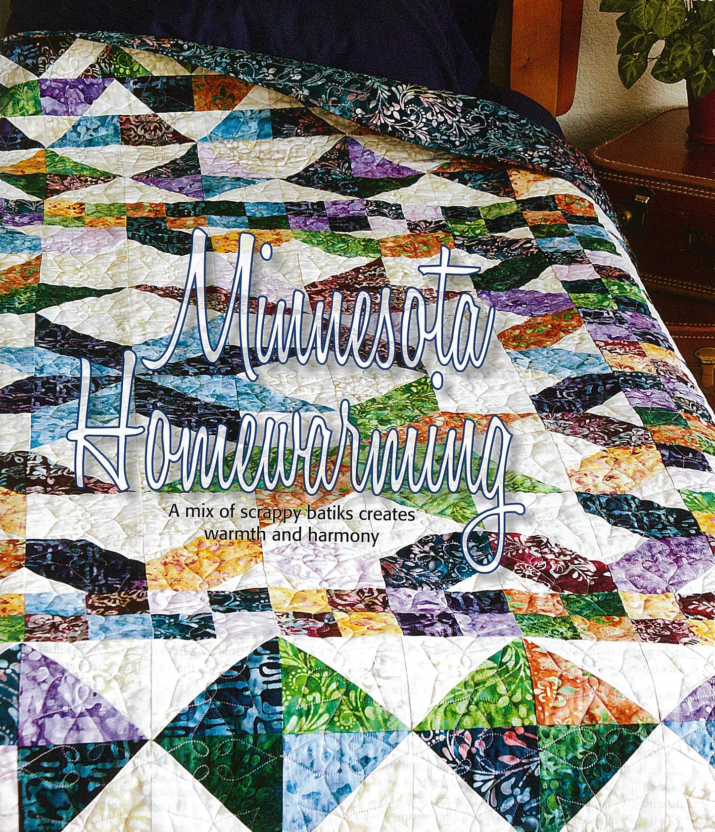 A vibrant geometric patchwork quilt from Devoted to Scraps—Best of Quiltmaker by Leisure Arts covers a bed. Overlaid text reads "Minnesota Homewarming," sparking warmth and inspiration for creative fabric projects.