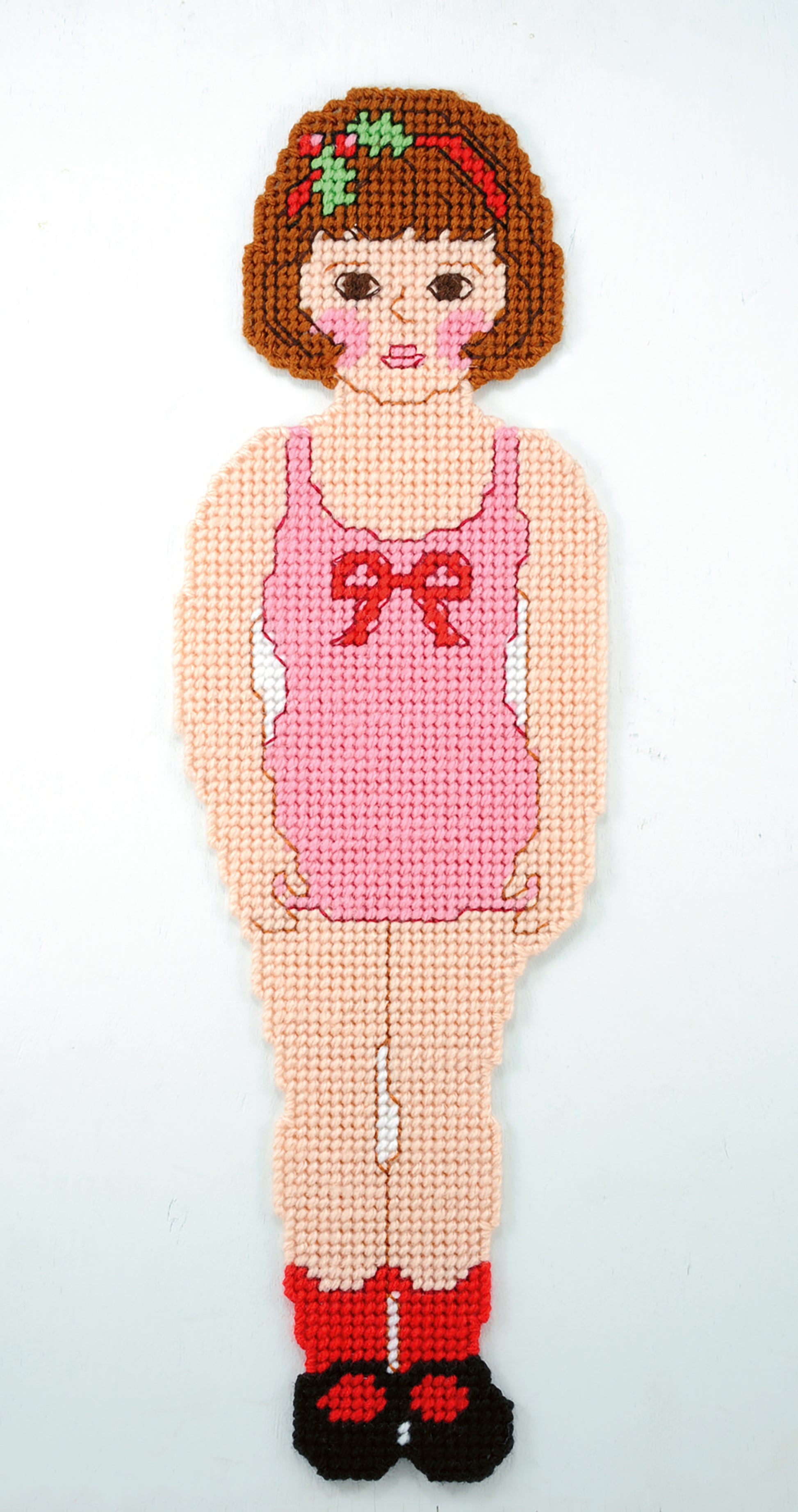 Paper Dolls by Leisure Arts features a pixel art-style girl with short brown hair in a pink dress with red bow and black shoes, cross-stitched on white—perfect for darling dolls or everyday outfits.