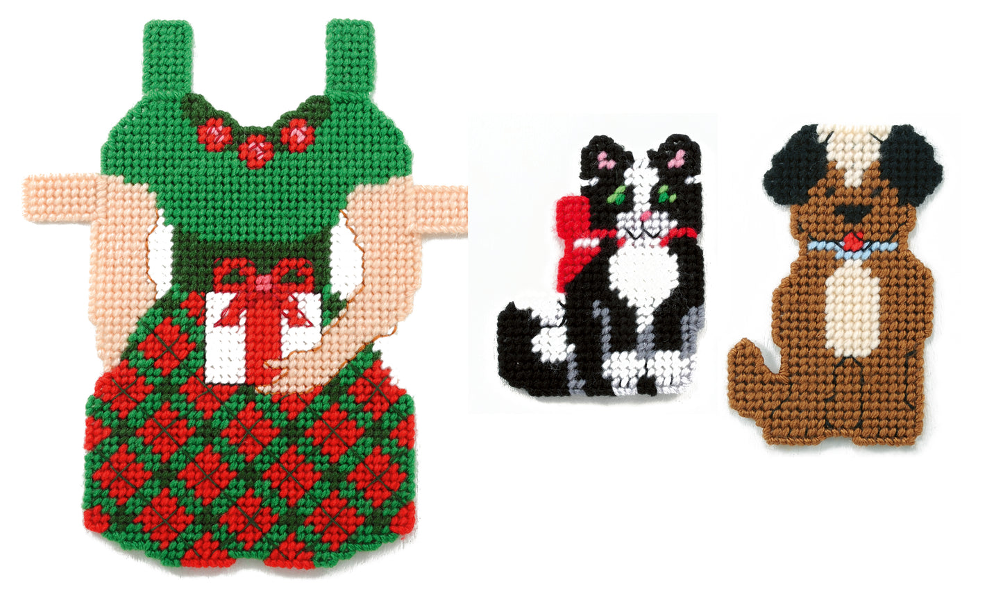 Three Paper Dolls by Leisure Arts: a person in a green and red dress with a gift, a black and white cat with a red bow, and a brown dog with dark ears, all shown on a white background.