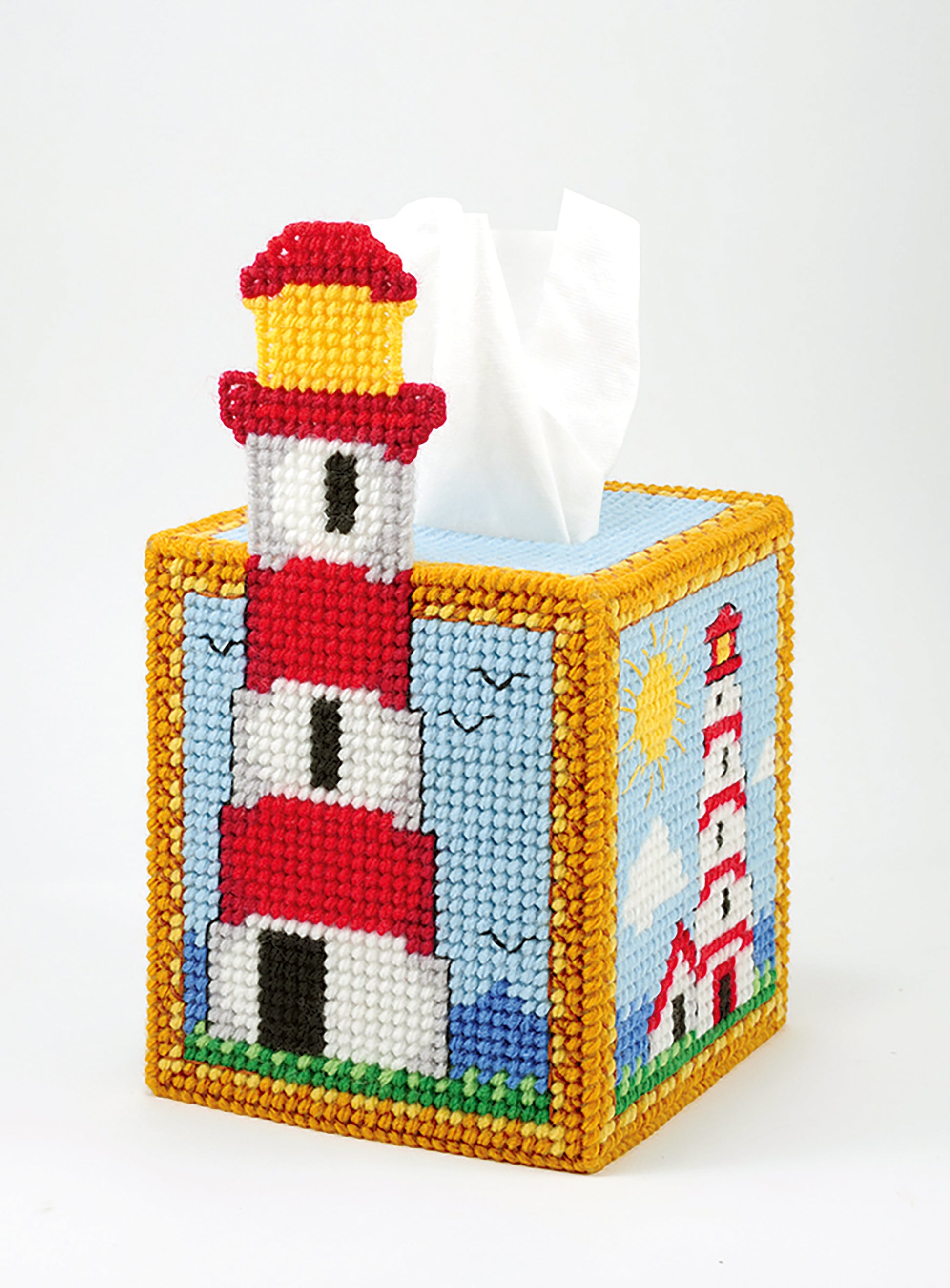 Leisure Arts’ “Tissue Box Covers—8 Projects to Brighten Up Any Room in Your Home” features plastic canvas designs like a 3D red-and-white lighthouse with a blue sky, clouds, and sun for bright coastal decor.
