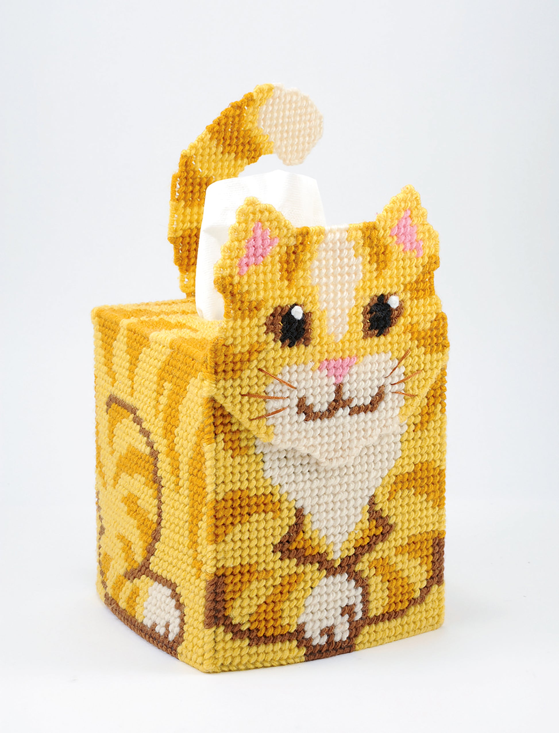 Brighten any room with Leisure Arts' "Tissue Box Covers—8 Projects," featuring a cute orange tabby cat design made with plastic canvas and yarn, complete with a tail loop and tissue emerging behind its head.