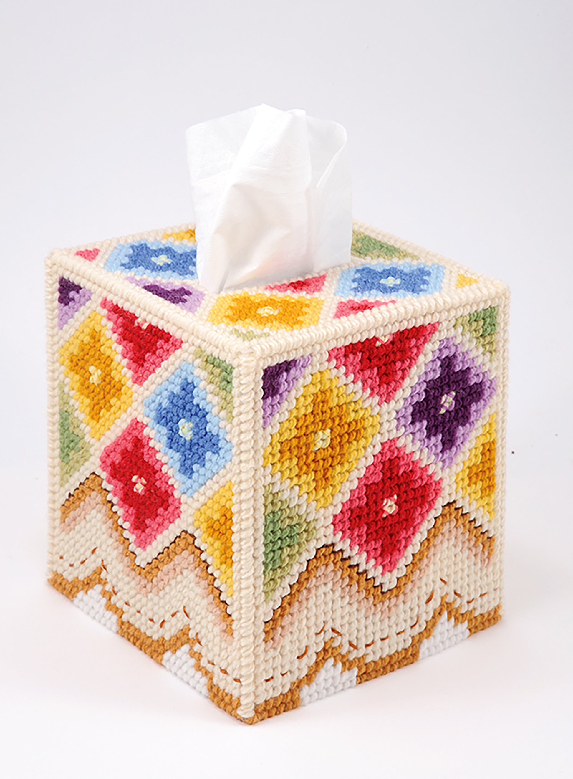 The "Tissue Box Covers—8 Projects to Brighten Up Any Room in Your Home" by Leisure Arts features a square cover with a colorful diamond pattern on cream, made with worsted weight yarn and plastic canvas, topped by a white tissue.