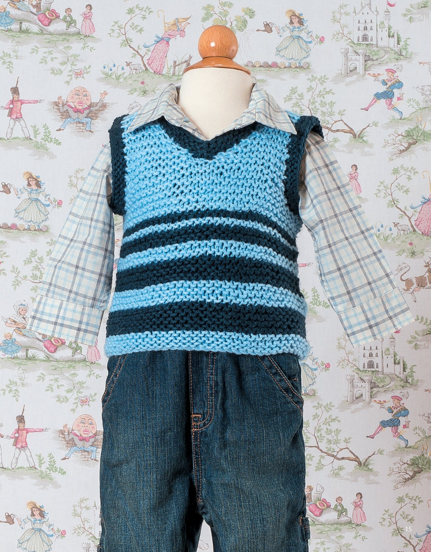 A child mannequin models an outfit featuring a garter stitch knitted vest from Garter Stitch for Baby by Leisure Arts, layered over a plaid shirt and jeans—set amid fairy tale wallpaper, it’s perfect inspiration for beginner knitters.