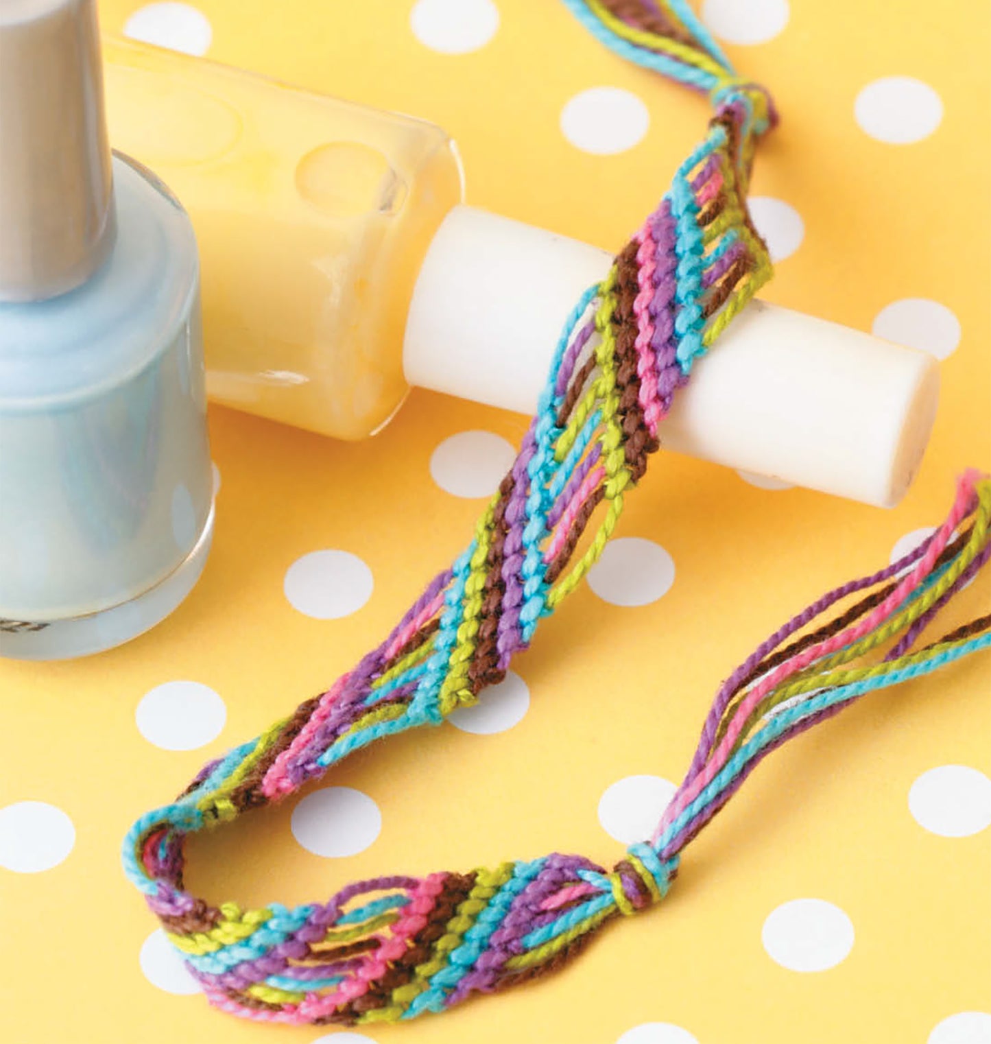 The Knots & Beads—Easy Jewelry to Make & Share! Digital Download from Leisure Arts is shown beside a light blue nail polish bottle on a yellow polka dot background, ideal for beginners in jewelry making.