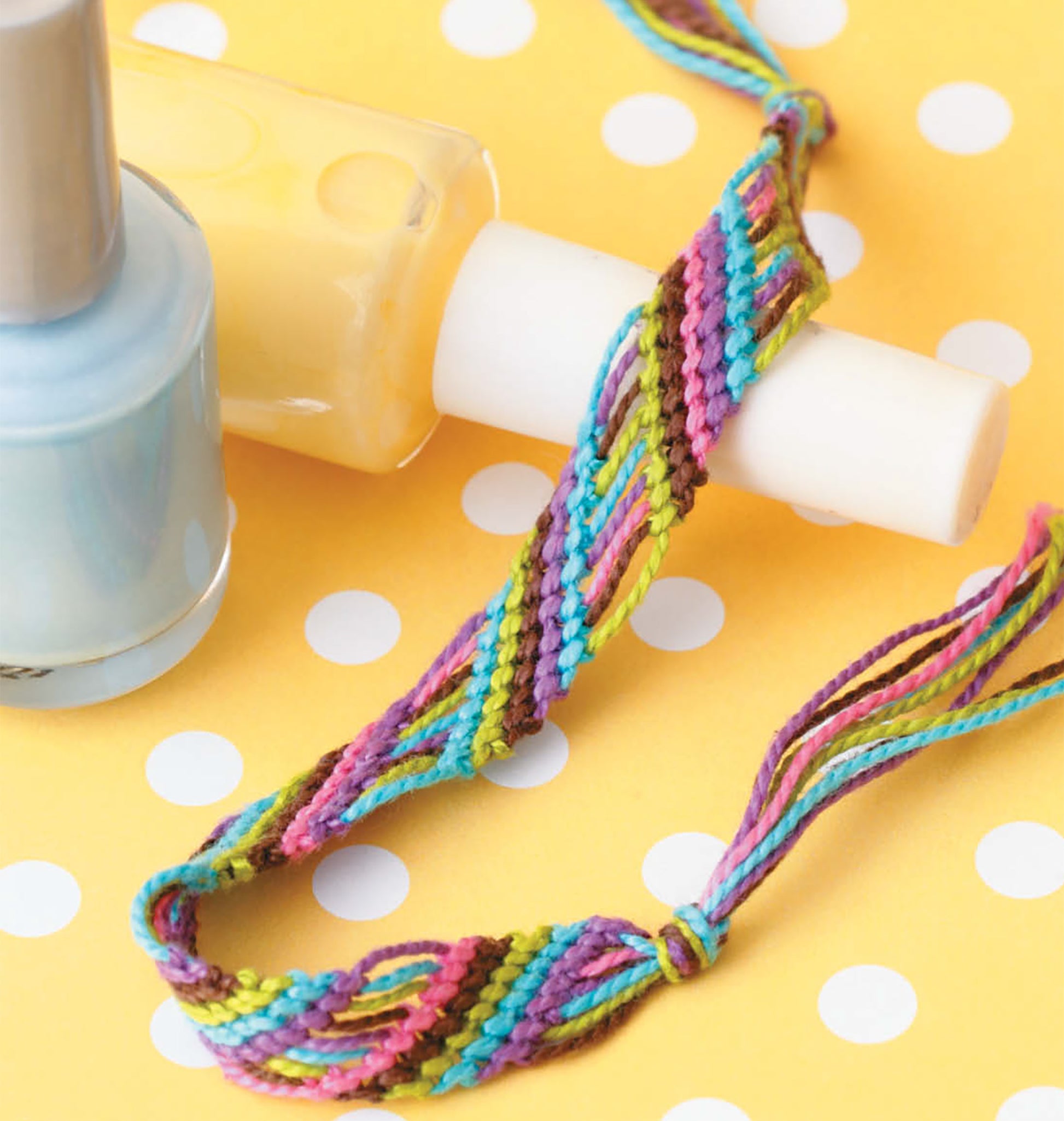 The Knots & Beads—Easy Jewelry to Make & Share! Digital Download from Leisure Arts is shown beside a light blue nail polish bottle on a yellow polka dot background, ideal for beginners in jewelry making.