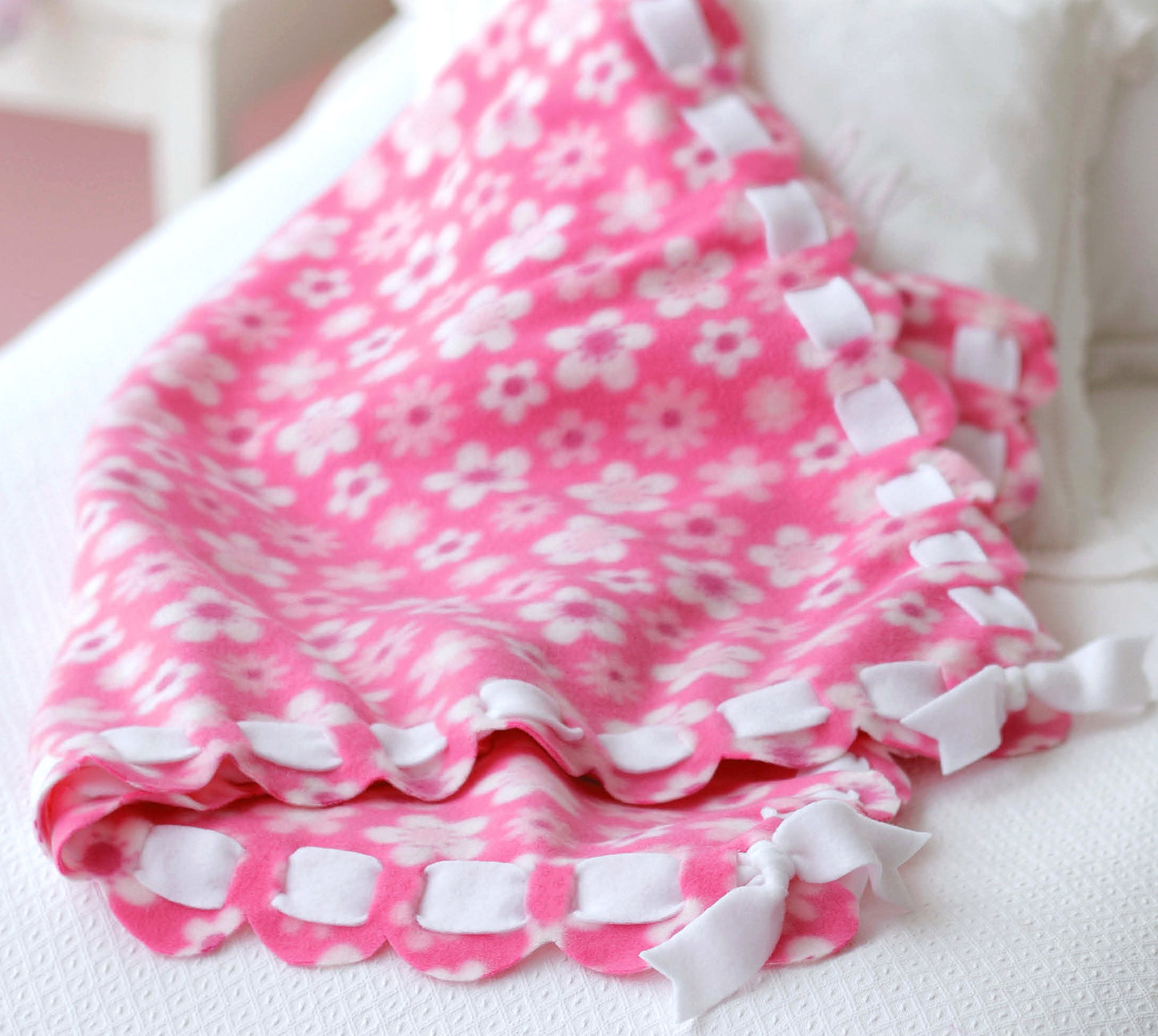 The Leisure Arts No-Sew Fleece Throws & Pillows kit lets you easily create cozy, pink fleece blankets with white daisy patterns and scalloped edges—perfect for home decor or beginner no-sew fleece projects and crafts.