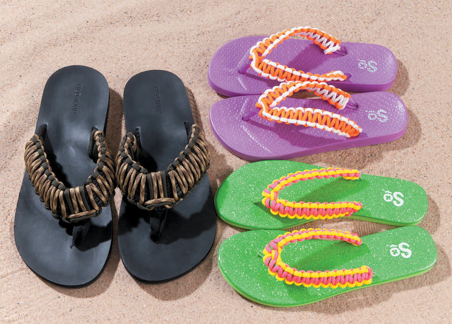 Three pairs of flip-flops on sand—black, purple with orange and white, and green with yellow and pink—all featuring braided straps inspired by Paracord Crafts from Leisure Arts.