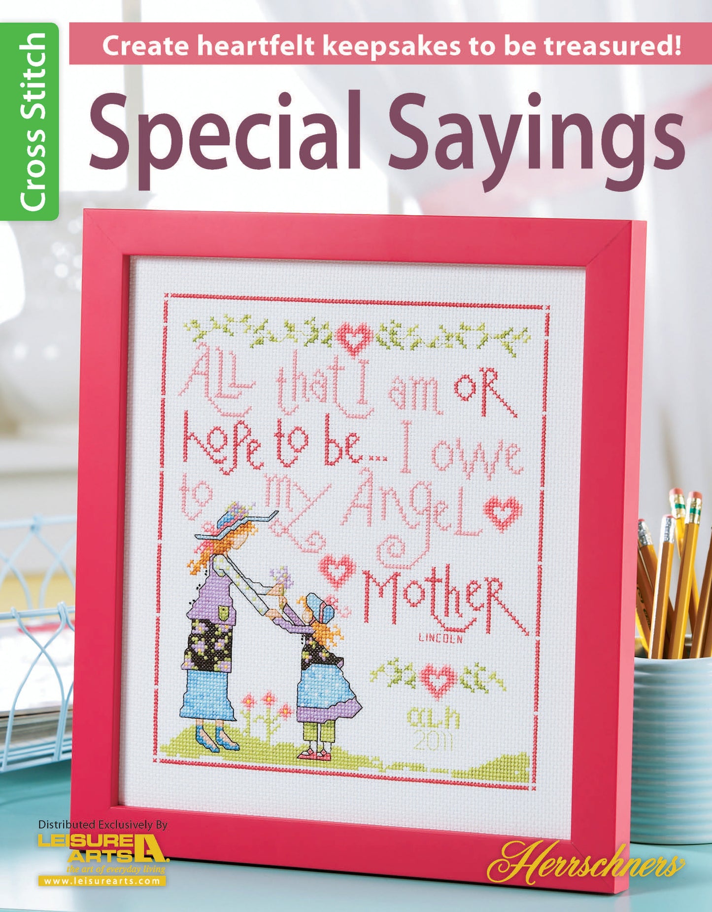The Leisure Arts Special Sayings Cross Stitch features a touching mother-child design with the quote, “All that I am or hope to be – I owe to my Angel Mother,” showcased in a pink frame as a heartfelt keepsake on a craft magazine cover.