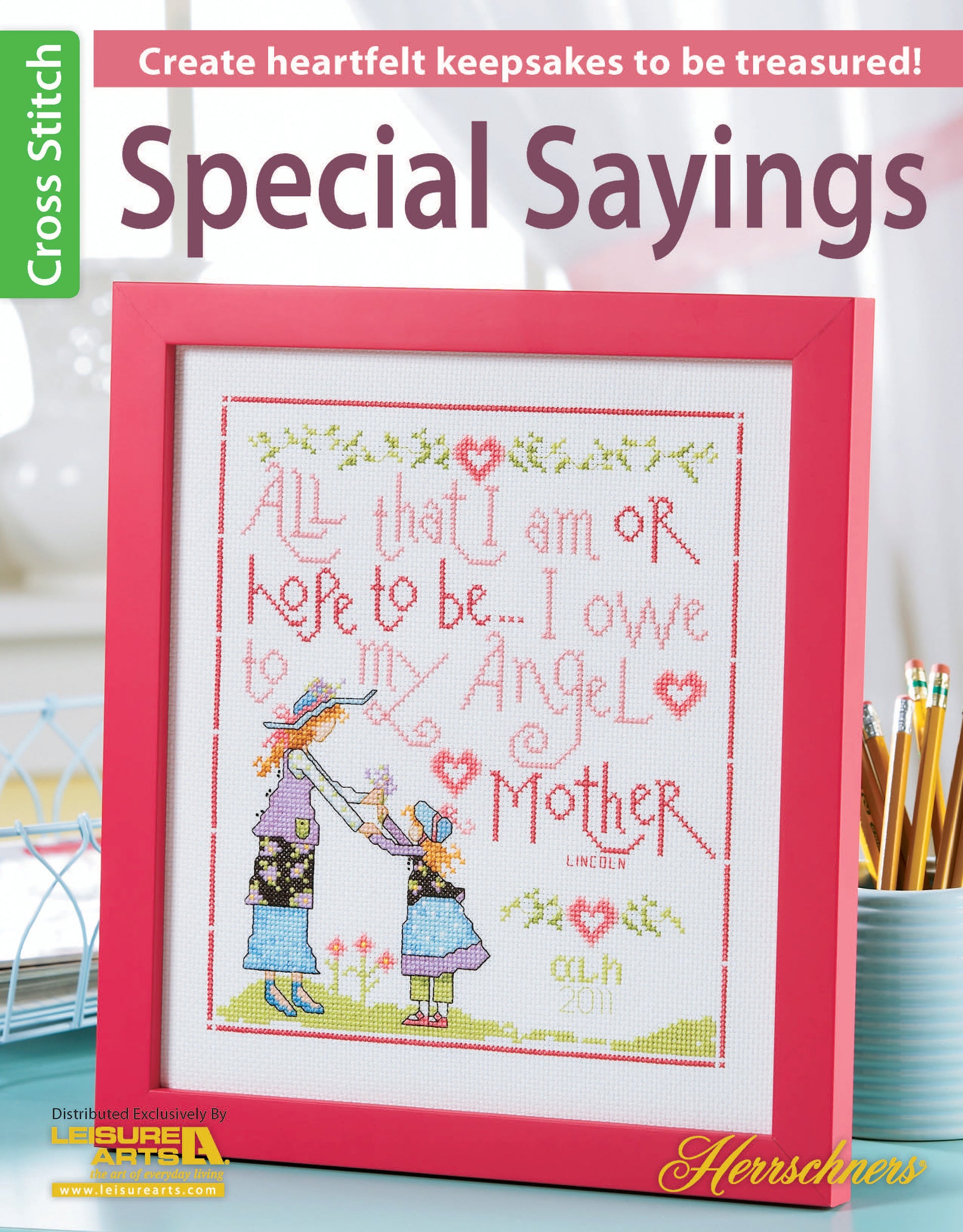 The Leisure Arts Special Sayings Cross Stitch features a touching mother-child design with the quote, “All that I am or hope to be – I owe to my Angel Mother,” showcased in a pink frame as a heartfelt keepsake on a craft magazine cover.