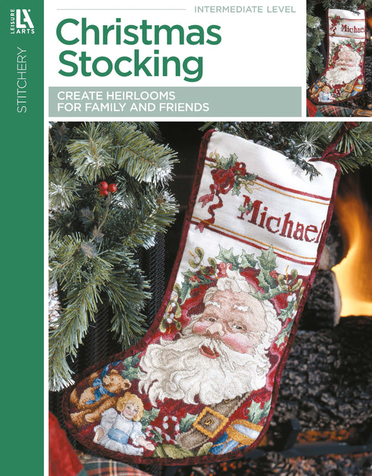 A cross stitch stocking hangs on a tree, featuring Santa, toys, and "Michael" at the top. The design is from Leisure Arts’ book "Christmas Stocking—Create Heirlooms for Family and Friends" for intermediate cross stitchers.
