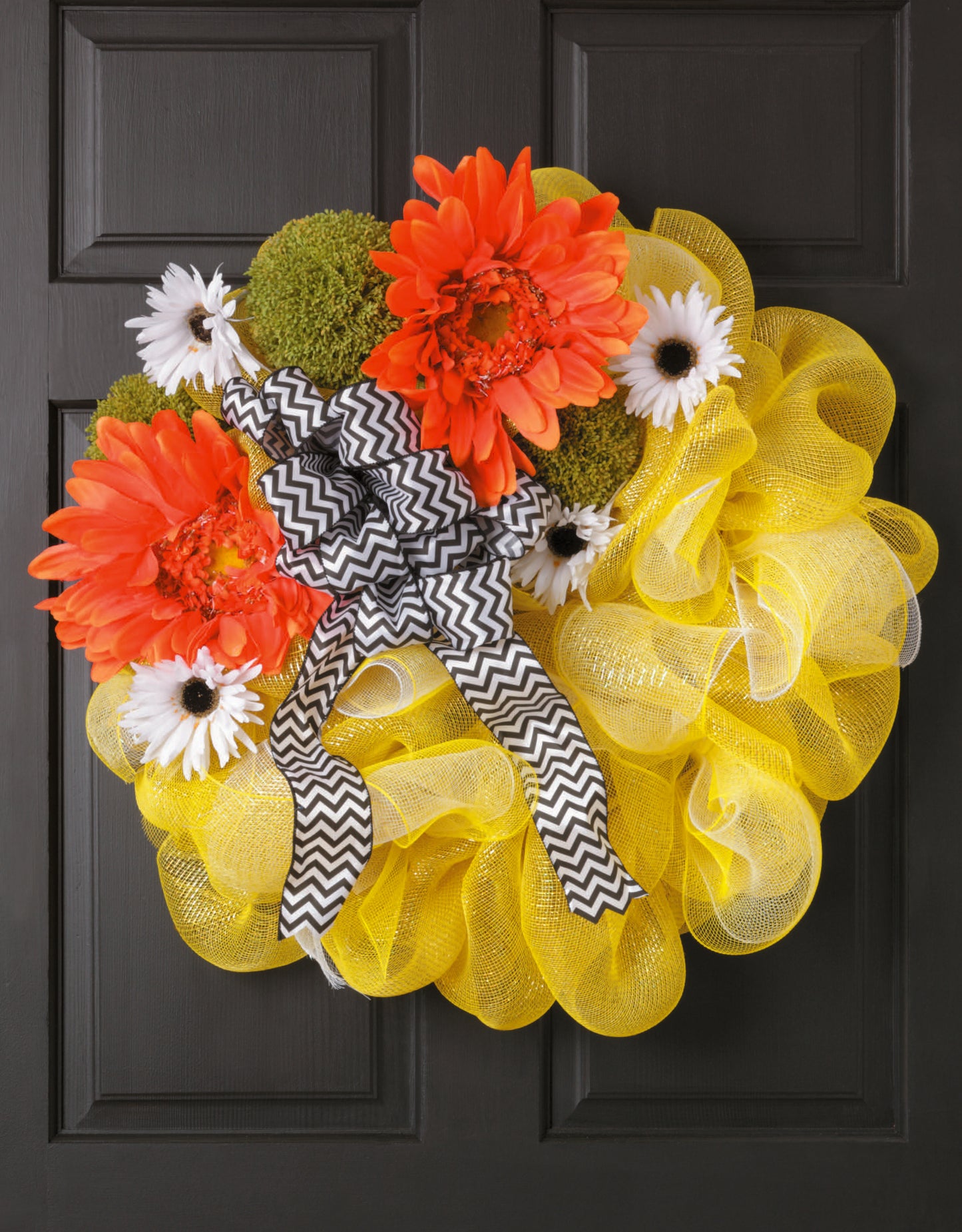Learn to Make Deco Mesh Wreaths by Leisure Arts features a wire frame adorned with orange and white flowers, green moss, a chevron ribbon, and yellow deco mesh—perfect as a stylish accent for your door.
