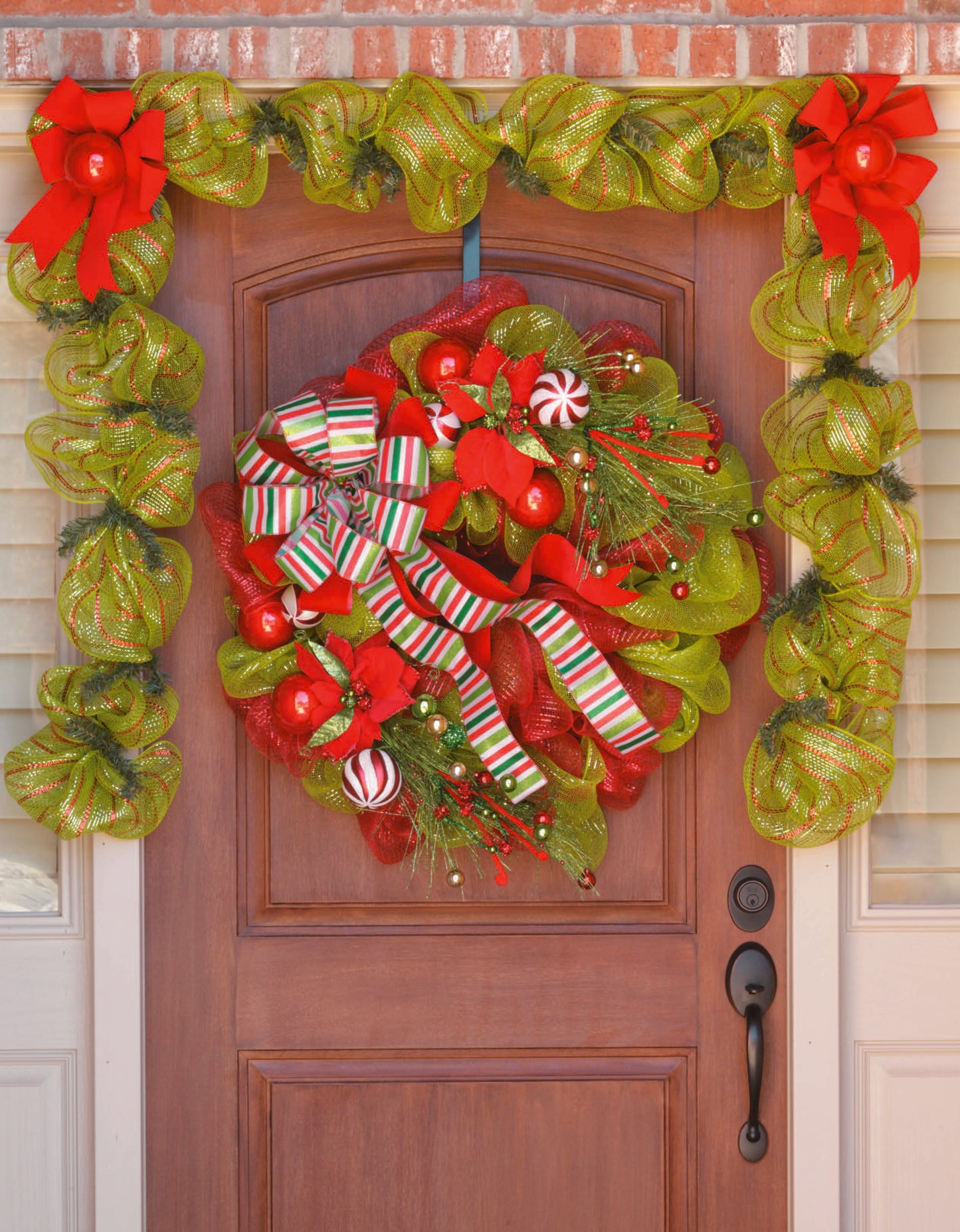 A front door features a festive Deco Mesh wreath made with red ornaments and striped ribbons, inspired by the "Learn to Make Deco Mesh Wreaths" kit from Leisure Arts for a cheerful holiday display.