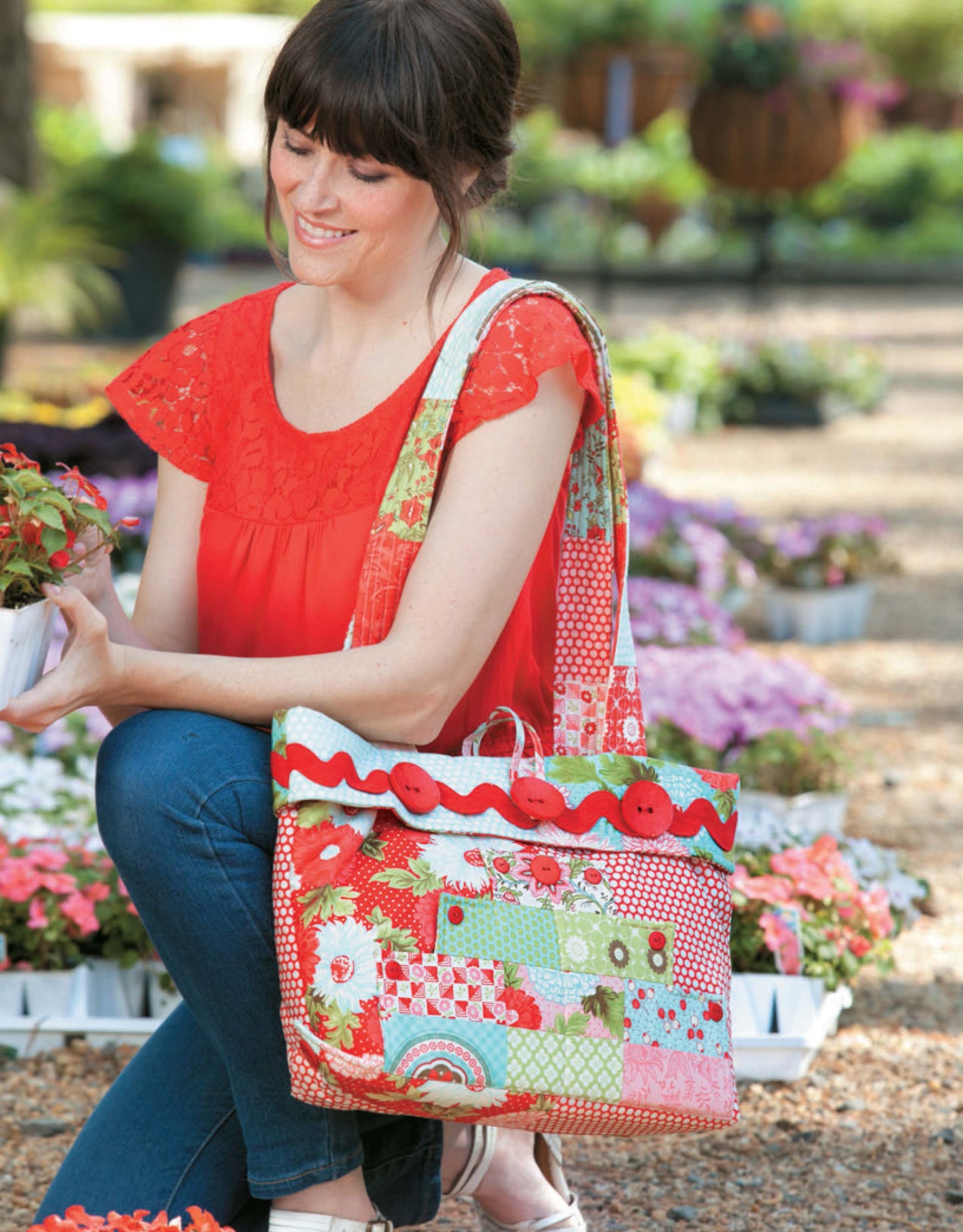 A woman outdoors among flowers holds a potted plant, with a colorful patchwork tote bag over her shoulder—made using fat quarters and accentuated with red buttons and trim. Pattern from the Sew Totes & Bags Digital Download by Leisure Arts.