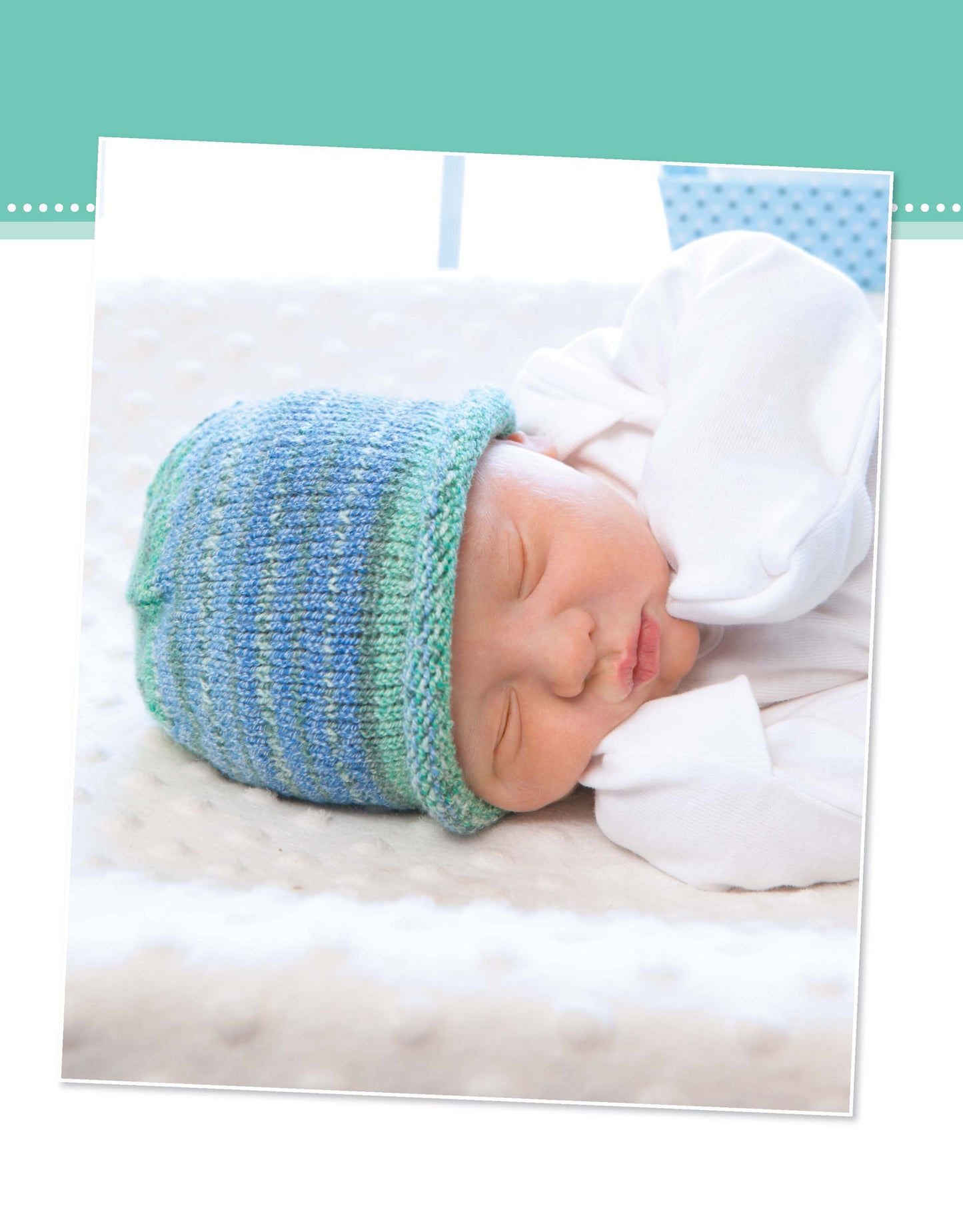 A newborn sleeps peacefully on a soft white blanket, wearing a blue and green hat made from Leisure Arts' "Projects for Baby Made with the Knook," with hands resting near their face.