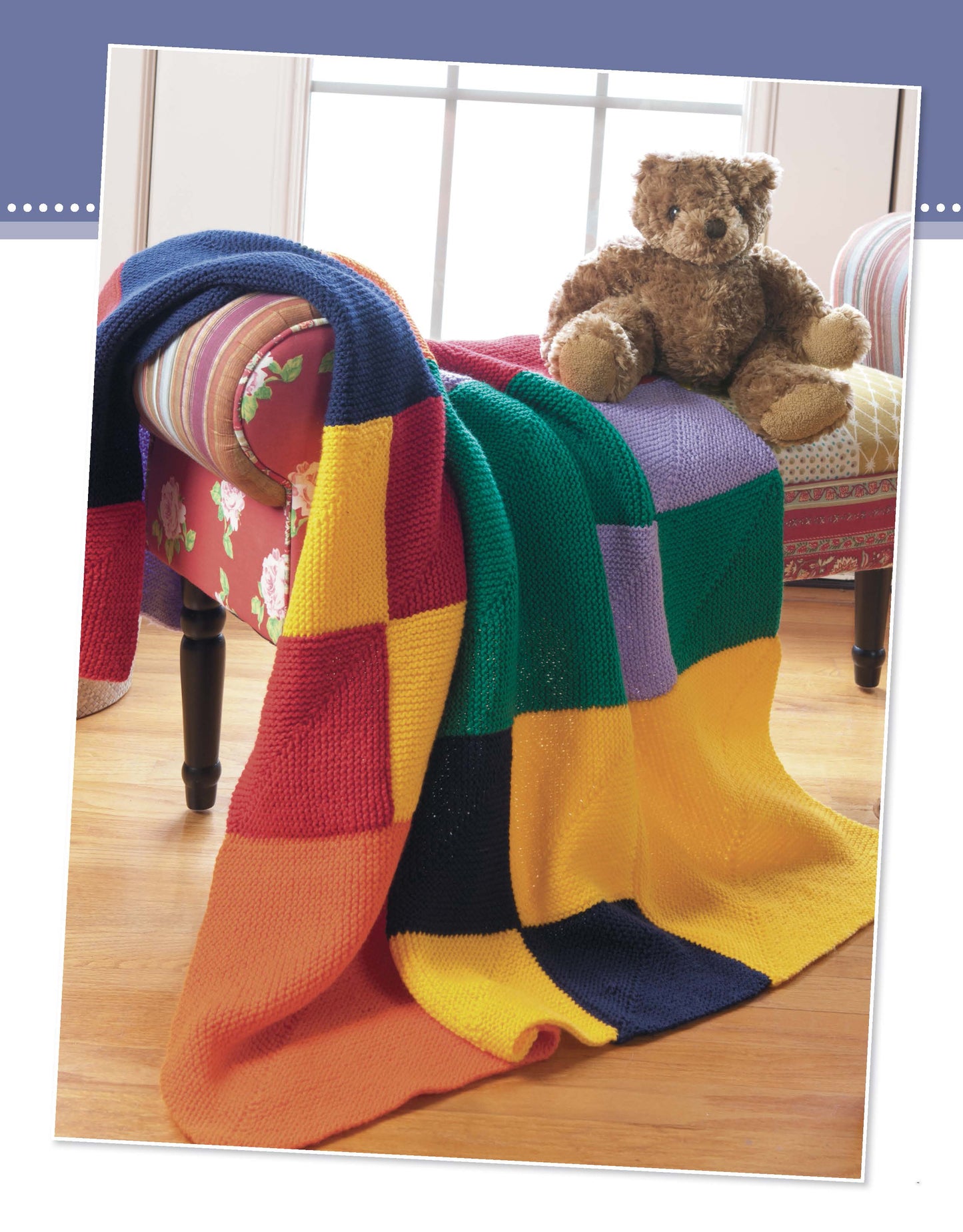 A vibrant patchwork blanket from "Projects for Baby Made with the Knook" by Leisure Arts, featuring bright squares, covers a colorful armchair where a brown teddy bear sits on a wooden floor. Perfect for beginner baby knitting projects.