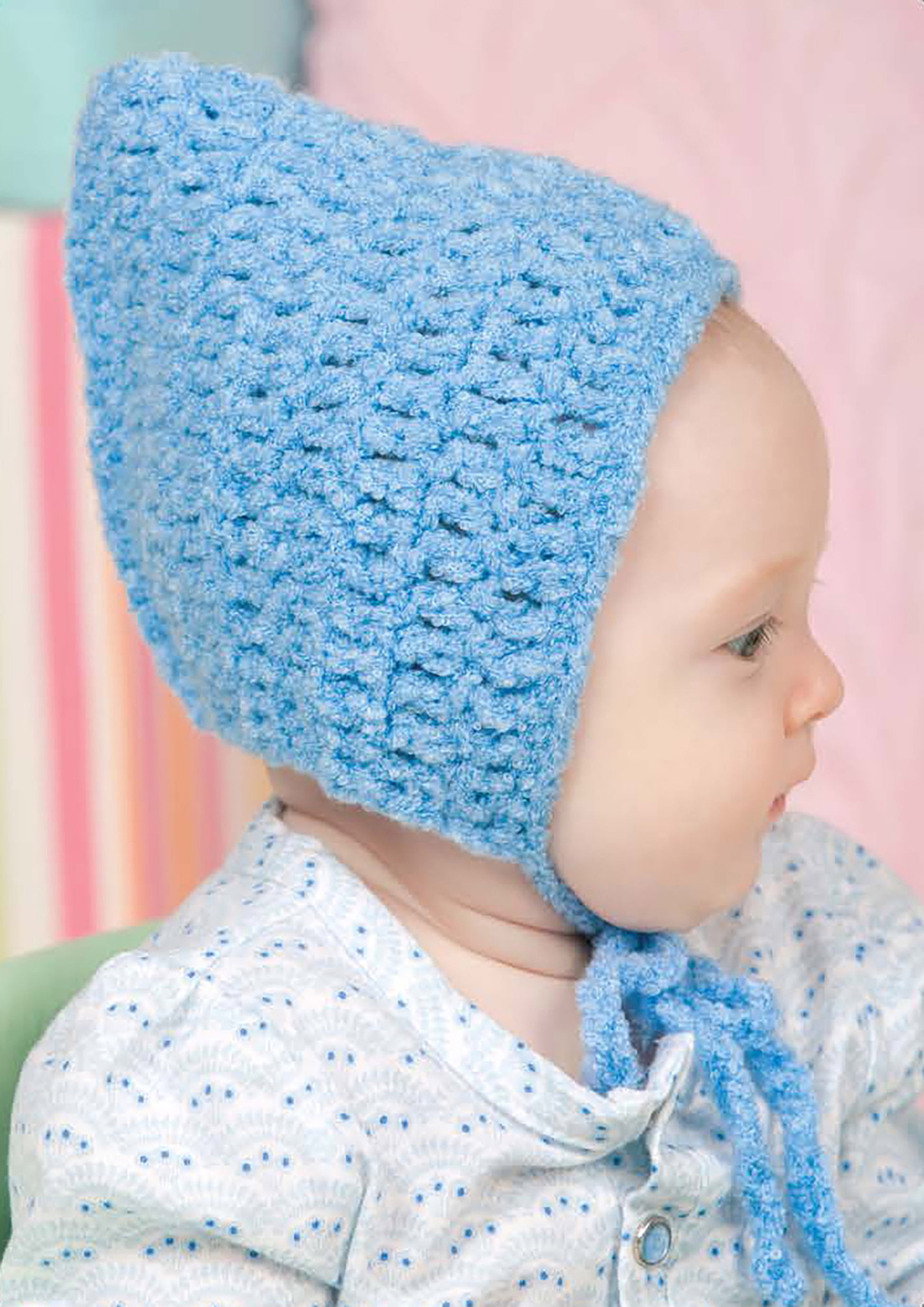 A baby wears a light blue knitted bonnet—perfect for beginner projects featured in "Baby Hats—10 Quick and Easy Patterns Written in Three Sizes" by Leisure Arts—paired with a white outfit, shown in profile against a soft background.
