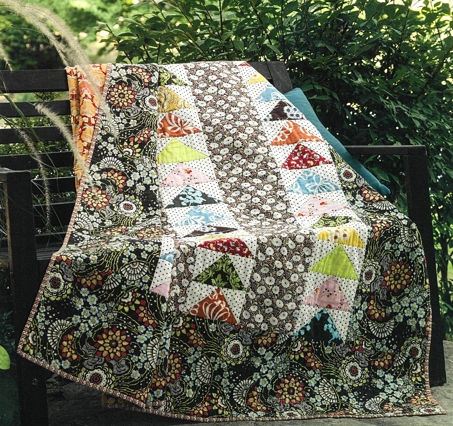 The Best of Quilty by Leisure Arts features a colorful quilt with floral and geometric patterns, draped over a wooden bench amid greenery—its decorative rows offer perfect inspiration for beginner or future embroidery projects.