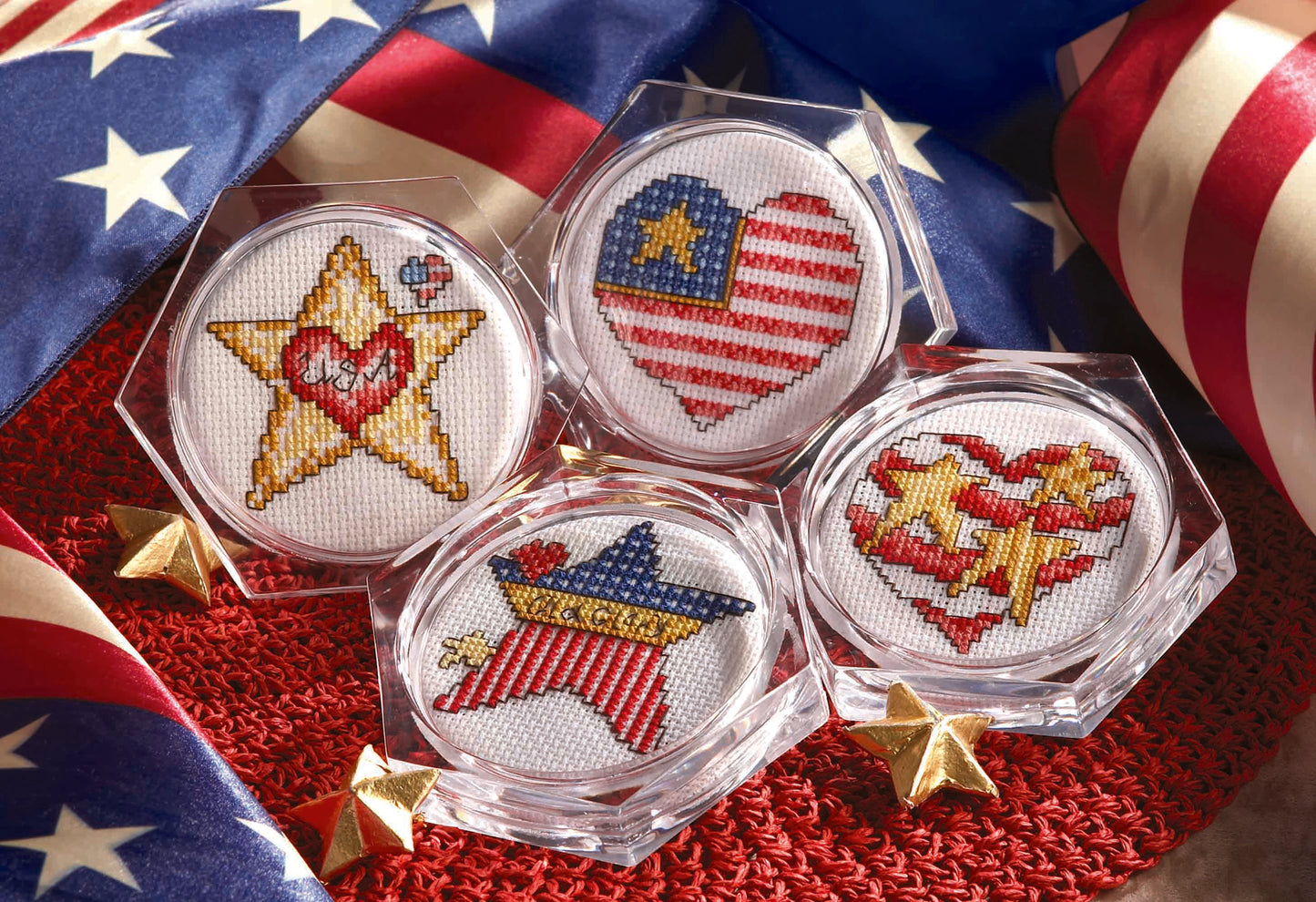 Seven beginner cross stitch coaster patterns from Leisure Arts' "Coasters—7 Cross Stitch Themes to Add Pizzazz to Your Home Decor" are displayed in clear frames with patriotic red, white, and blue designs on an American flag-themed background.