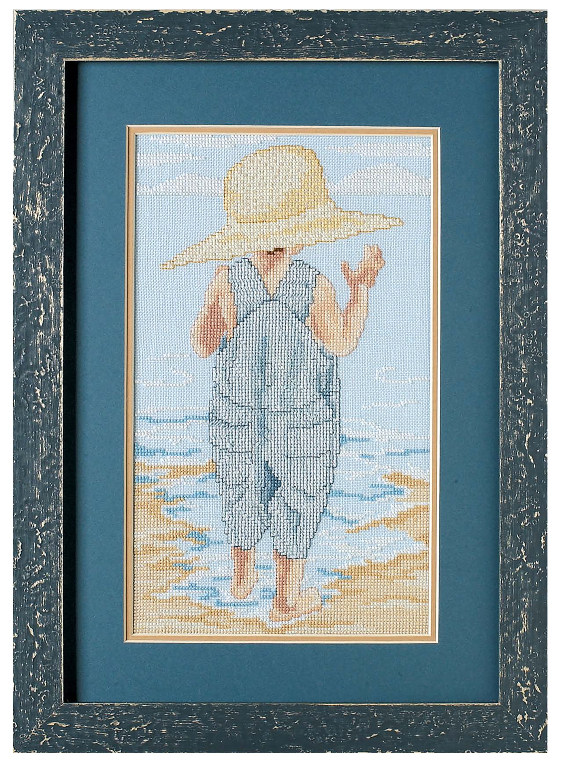 The Seaside Portraits Cross Stitch by Leisure Arts features a young child in blue overalls and straw hat, standing barefoot on a beach—a charming framed embroidery for your home accents collection.