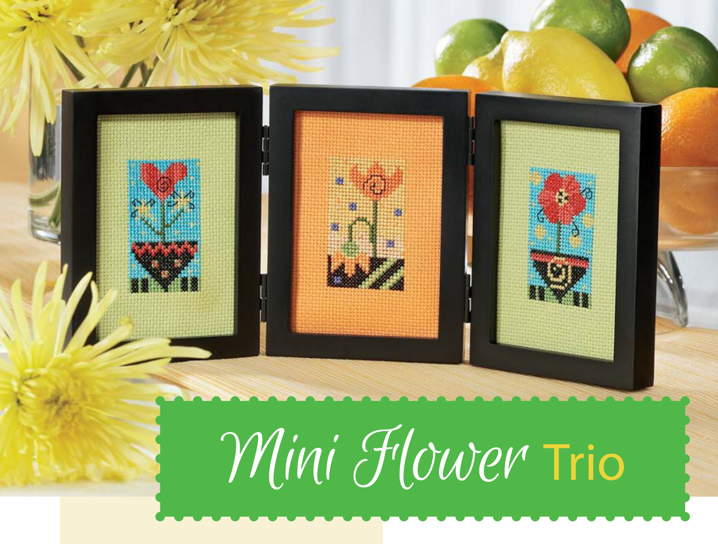 Three framed "Bright Blooms Cross Stitch" designs by Leisure Arts are displayed side by side with yellow flowers and a fruit bowl in the background. Text reads Mini Flower Trio, featuring whimsical floral patterns.