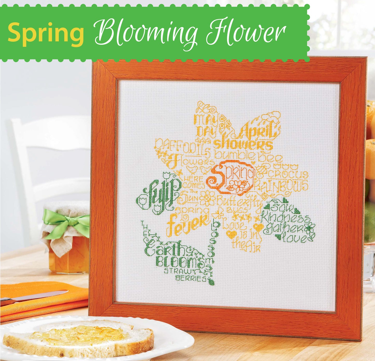 The Leisure Arts Seasonal Wordplay Cross Stitch Digital Download features a flower-shaped word cloud in green, yellow, and orange on 14 count Aida fabric—ideal as home decor. Displayed beside bread and a plant with "Spring Blooming Flower" above.