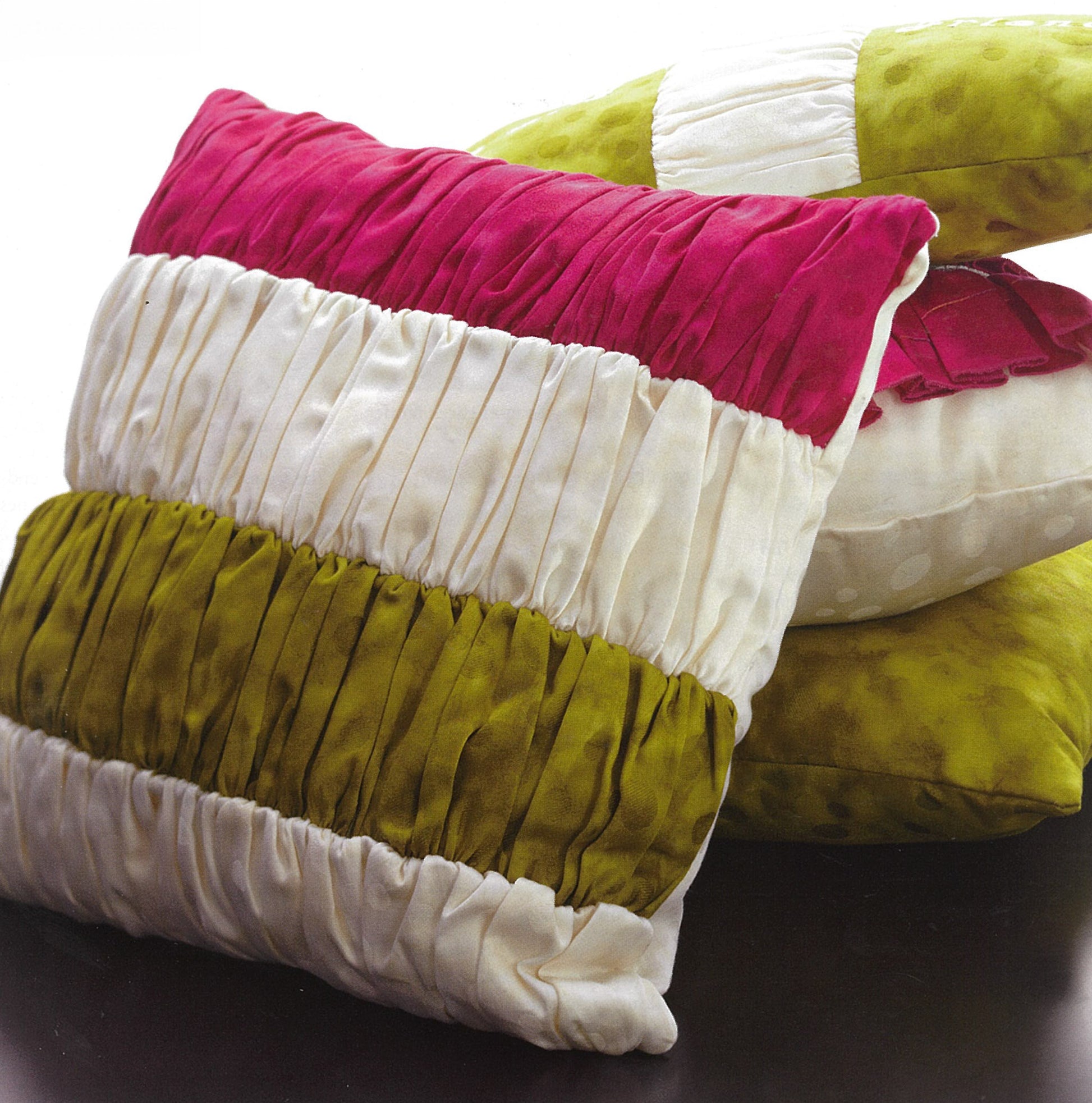 A magenta, white, and olive green pleated pillow from Leisure Arts' "Pillows—Accent Your Home with Plush Comfort & Style!" rests before two matching ones—ideal inspiration for your next sewing project.