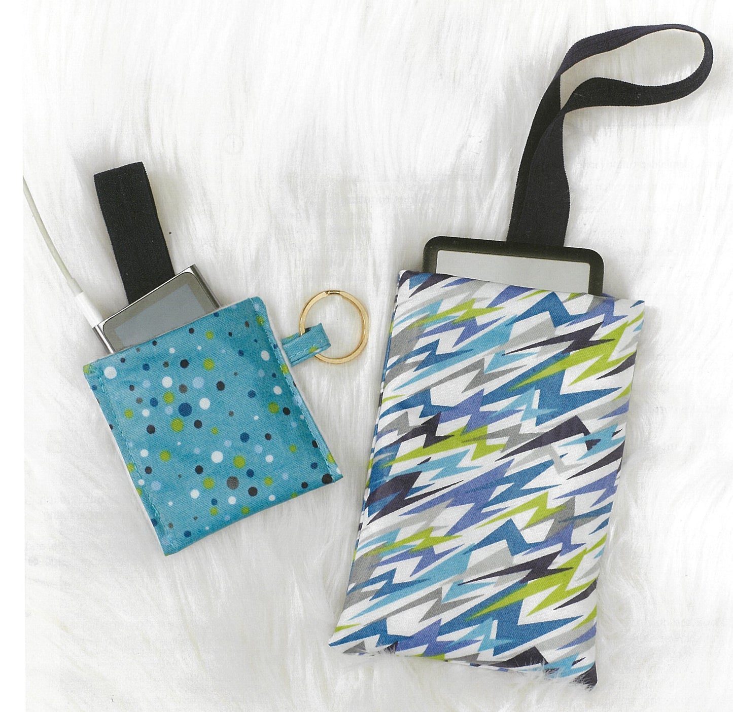 Two fabric pouches made with Sew it All: Quick Projects by Leisure Arts rest on a white textured surface. One is blue with polka dots; the other has a blue, green, and white geometric pattern. Both have keyrings and fit electronic devices.