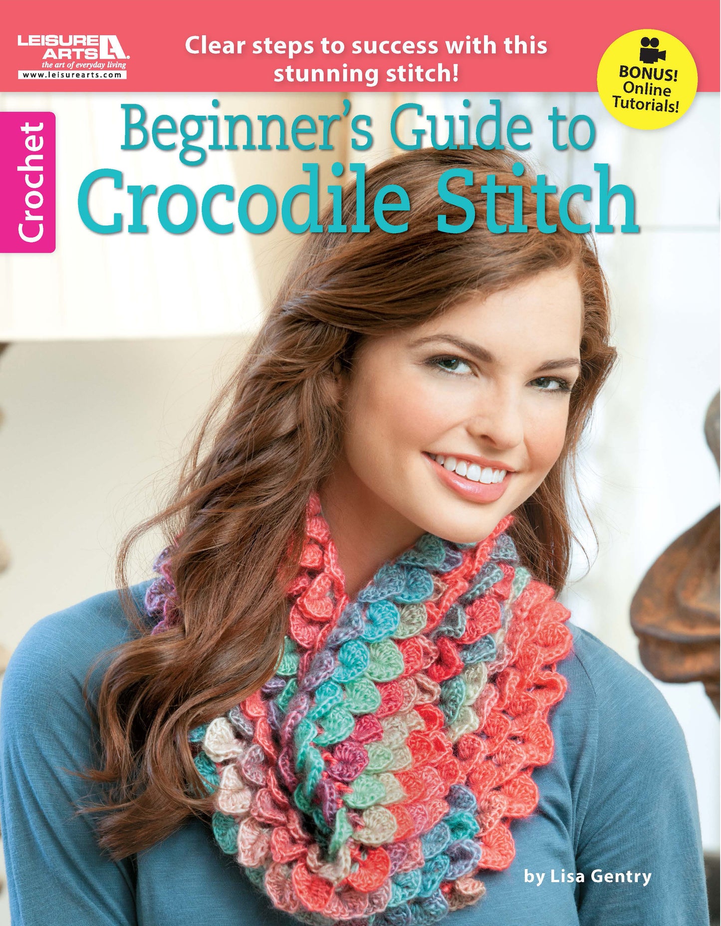 A smiling woman with long brown hair models a colorful scarf made with Crocodile Stitch on the cover of Leisure Arts’ "Beginner's Guide to Crocodile Stitch"—an ideal resource for new crocheters seeking inspiration.