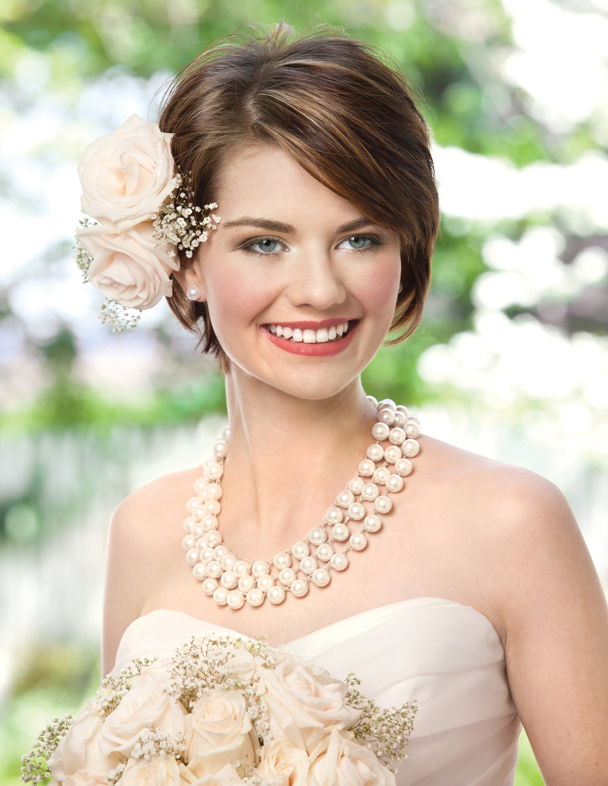 A smiling bride with short brown hair and cream roses wears a strapless gown and the beaded "Formal Jewelry—Crochet With Beads for Extra-Easy Glamour!" by Leisure Arts; she holds white roses, outdoors amid green foliage.