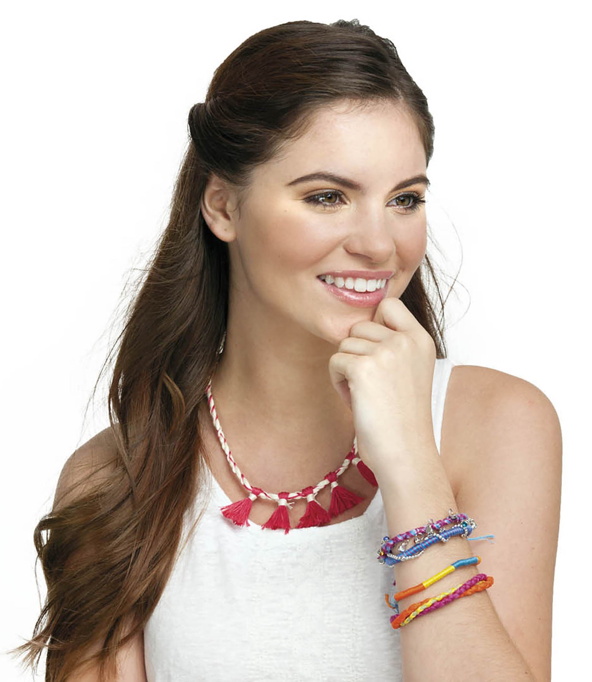 A woman with long brown hair wears a white top, a red tassel necklace, and colorful woven bracelets—wonderful inspiration for creative projects from Amazing Jewelry Made Easy by Leisure Arts—as she smiles and rests her chin on her hand.