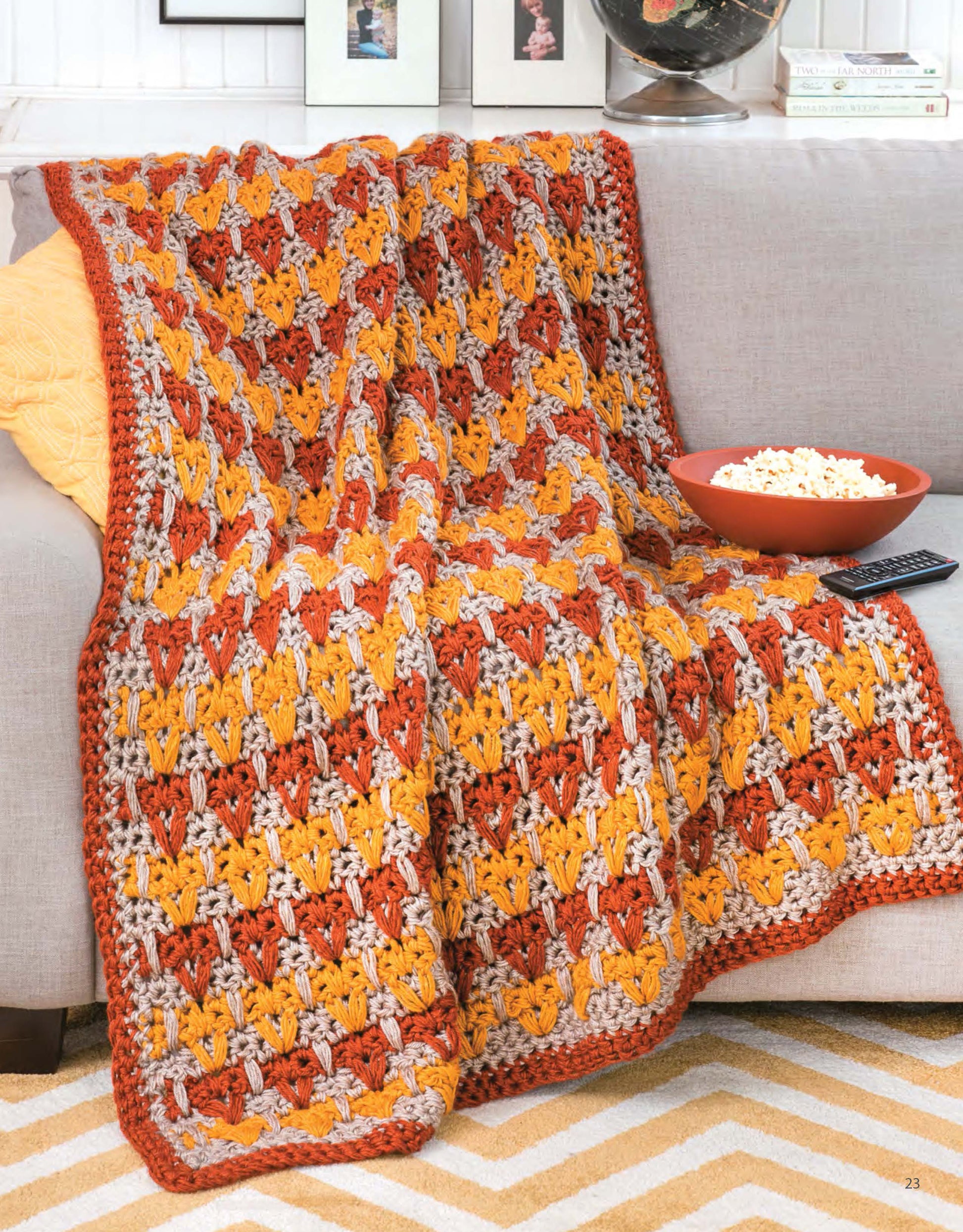 The Q-Hook Afghans for the Family digital download by Leisure Arts features crocheted blankets in orange, yellow, and beige tones with textured stitches, perfect for draping over a light gray sofa.
