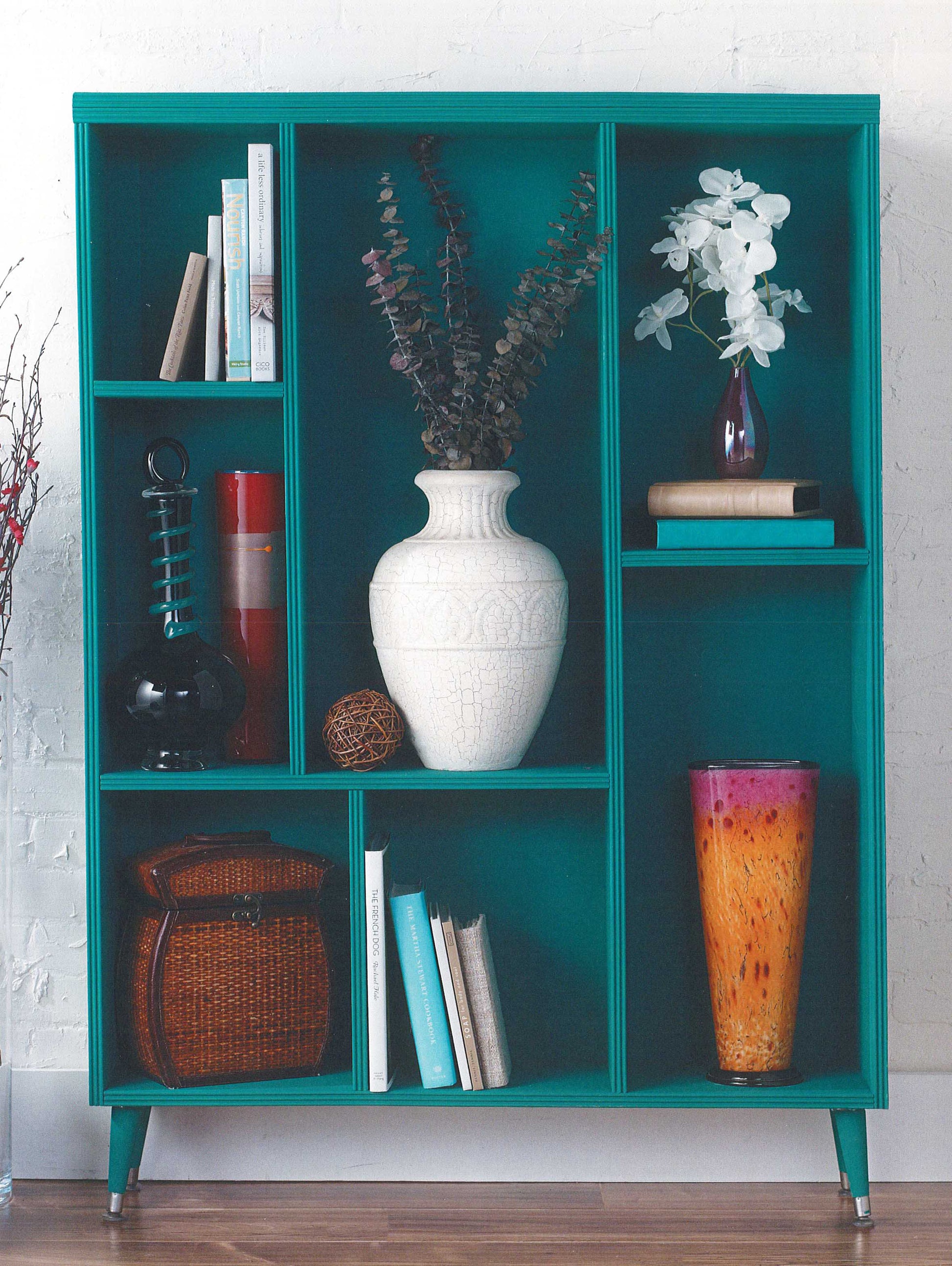 Show off your chalk painting skills from "A Beginner's Guide to Chalk Painting" by Leisure Arts with a teal bookshelf, books, vases, baskets, and more—an eye-catching display against a crisp white wall.