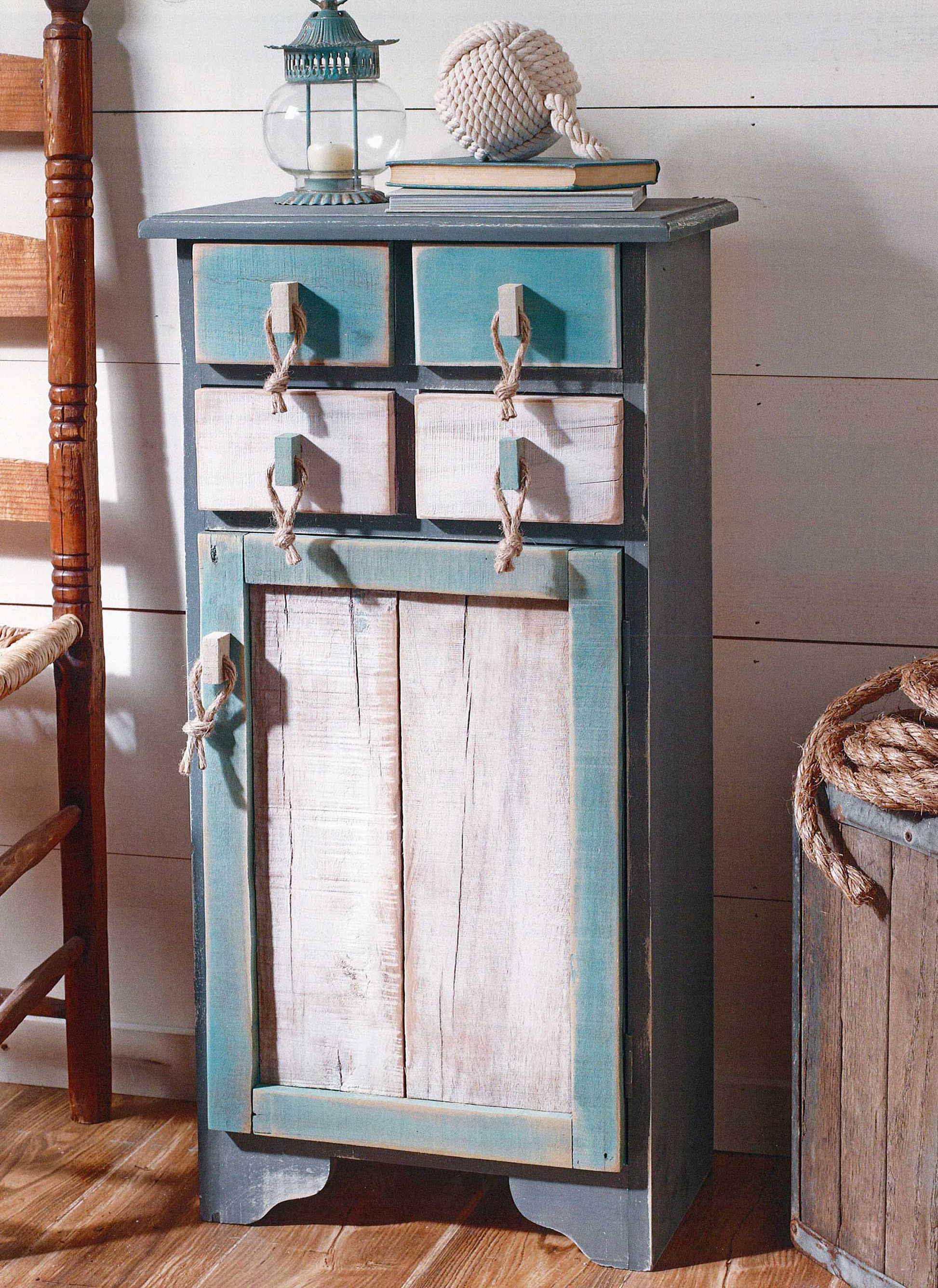 A rustic coastal cabinet with blue and white distressed finishes—created using tips from Leisure Arts' "A Beginner's Guide to Chalk Painting"—features rope handles, topped with nautical decor like a glass lantern and knotted rope ball.
