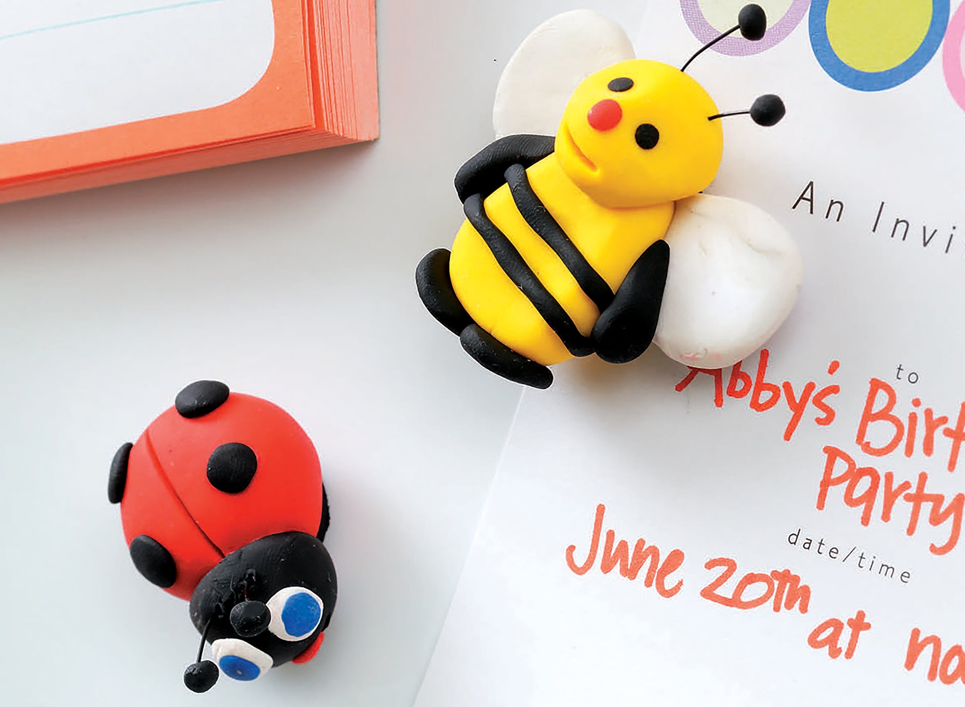 Two vibrant polymer clay figures—a yellow bee and a red ladybug—are featured with a birthday invitation and notepad in Clay Creations for All by Leisure Arts, making it perfect for beginner crafting projects.