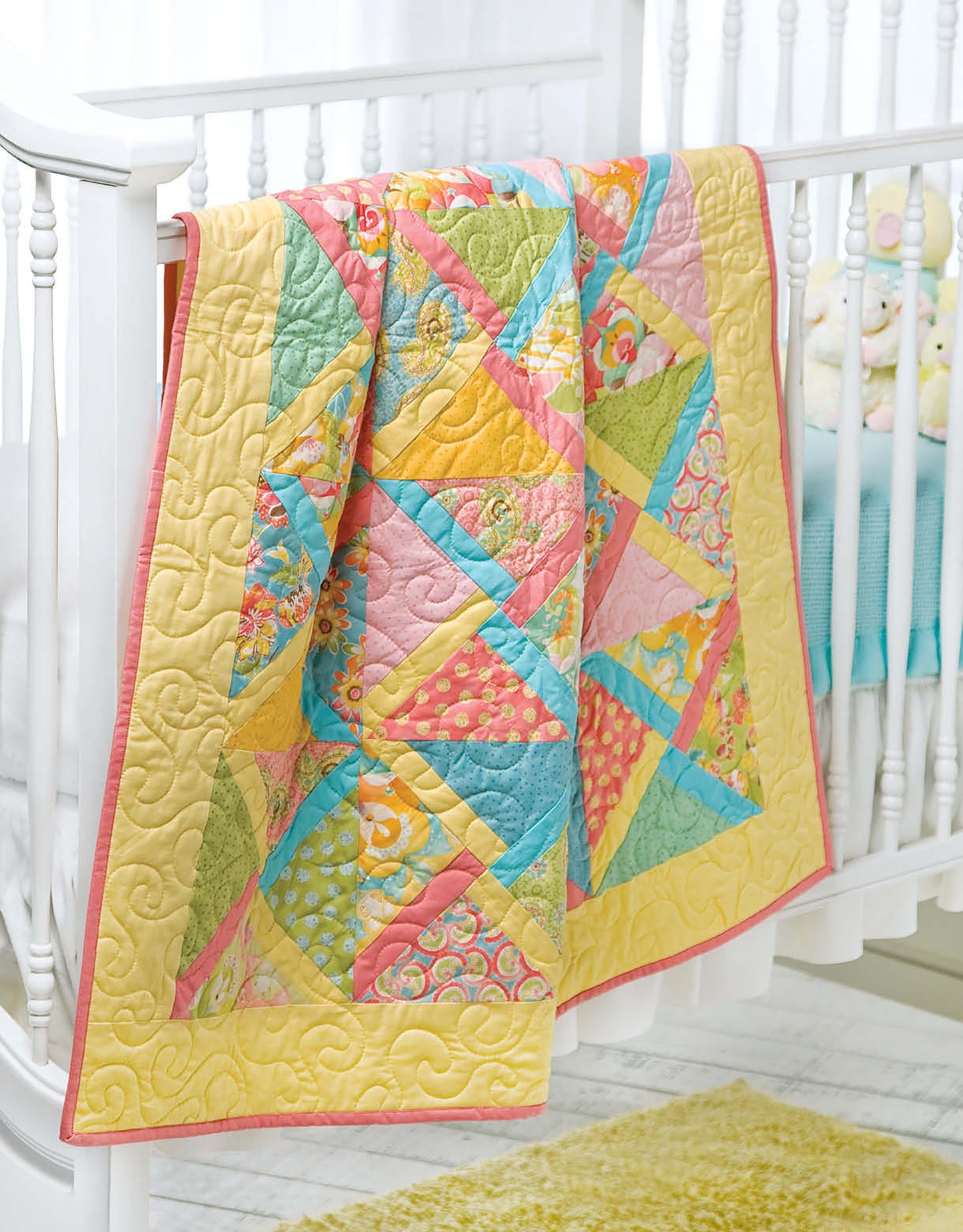 The Leisure Arts Baby Bright Quilts—Use Pops of Color in Stunning Baby Designs! features yellow, pink, green, and blue patterns draped over a white crib, adding vibrant charm to any nursery.
