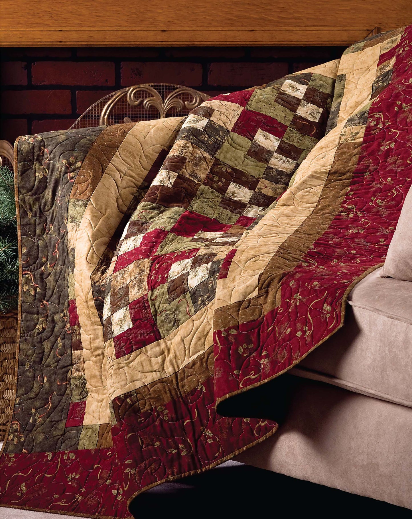 The “Quick & Easy Quilts” by Leisure Arts is a patchwork quilt in red, green, beige, and brown with floral squares—ideal for beginner quilt patterns or fat quarter quilts—displayed on a beige sofa beside a brick wall and woven basket.