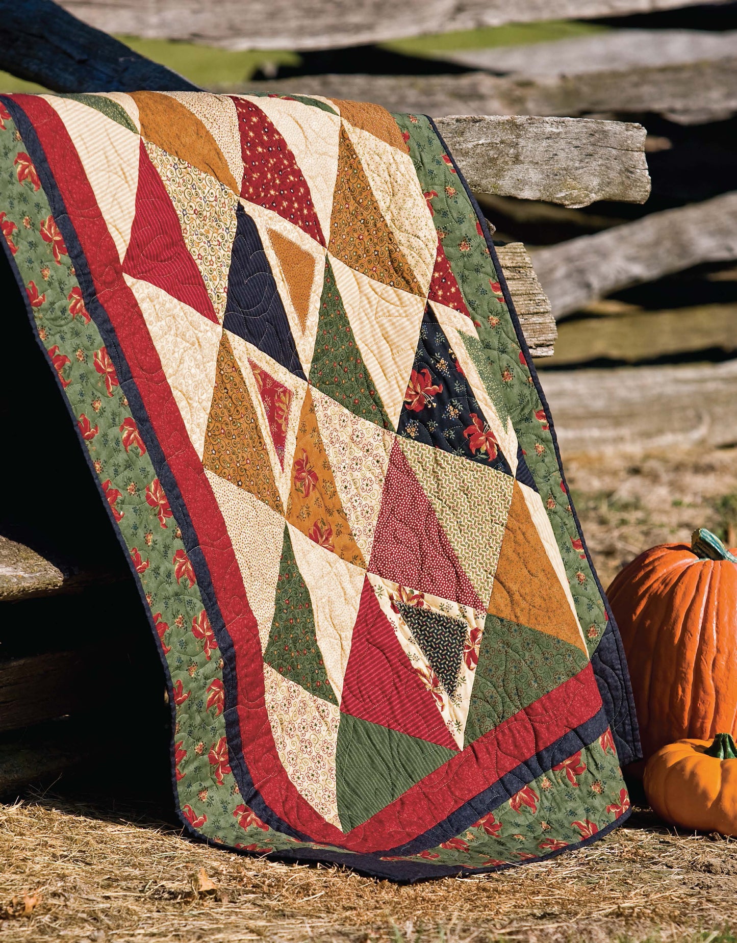 The Lap & Throw Quilts by Leisure Arts features a vibrant triangle patchwork in red, green, gold, and beige draped over a rustic wooden fence with an orange pumpkin nearby—perfect inspiration for beginner quilting projects.